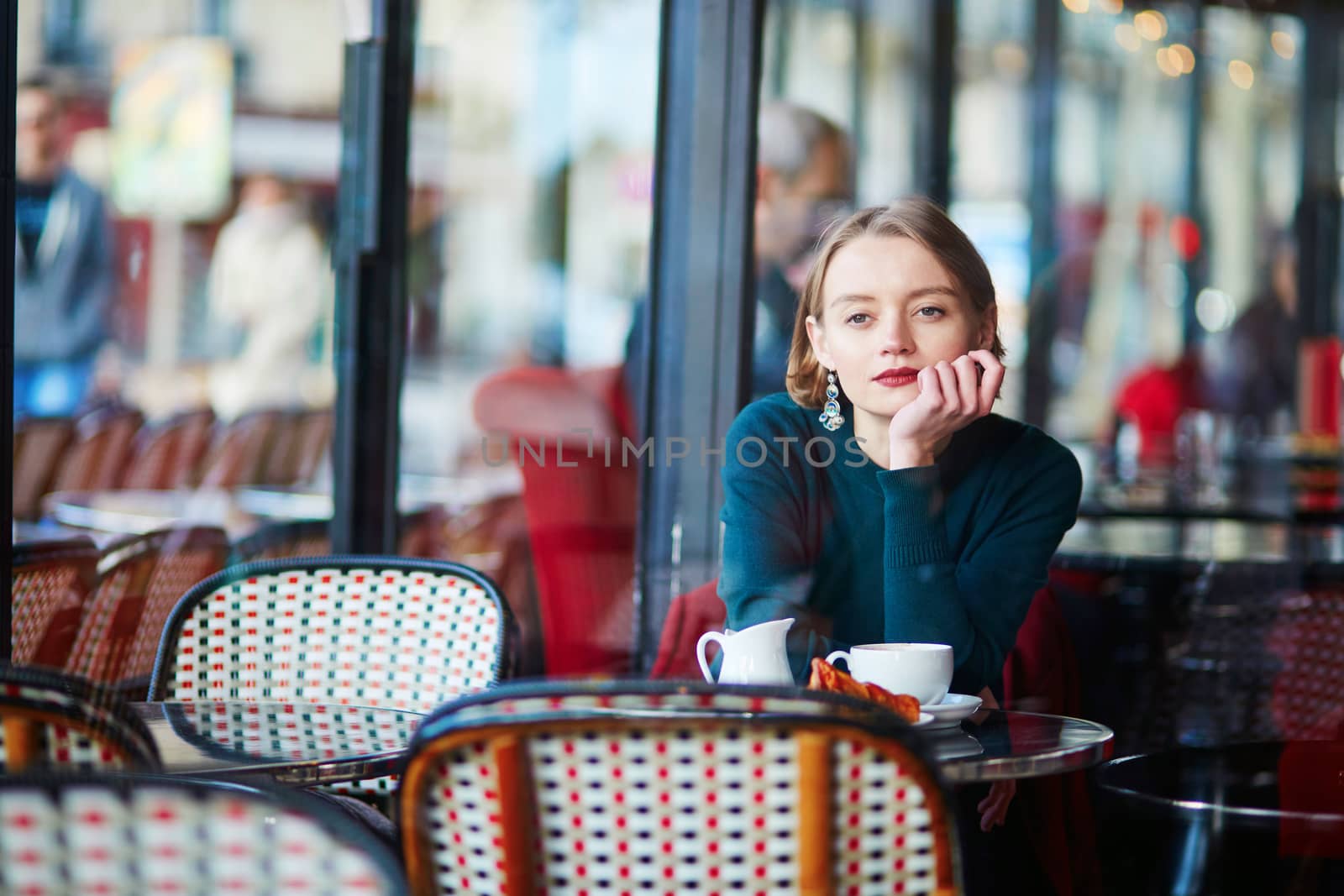 Young elegant woman drinking coffee and using her mobile phone in traditional cafe in Paris, France