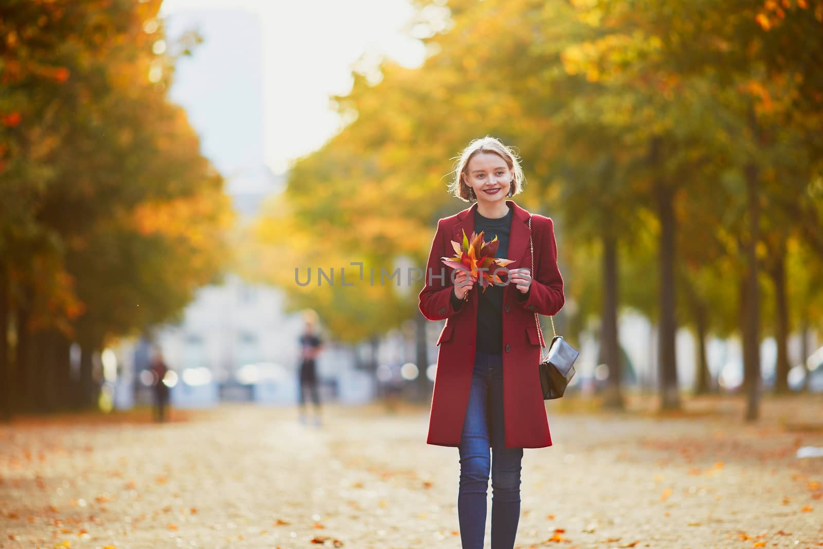 Beautiful young woman with bunch of colorful autumn leaves walking in park on a fall day