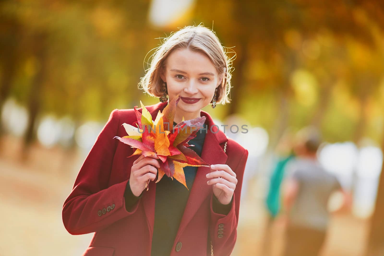 Beautiful young woman with bunch of colorful autumn leaves walking in park on a fall day