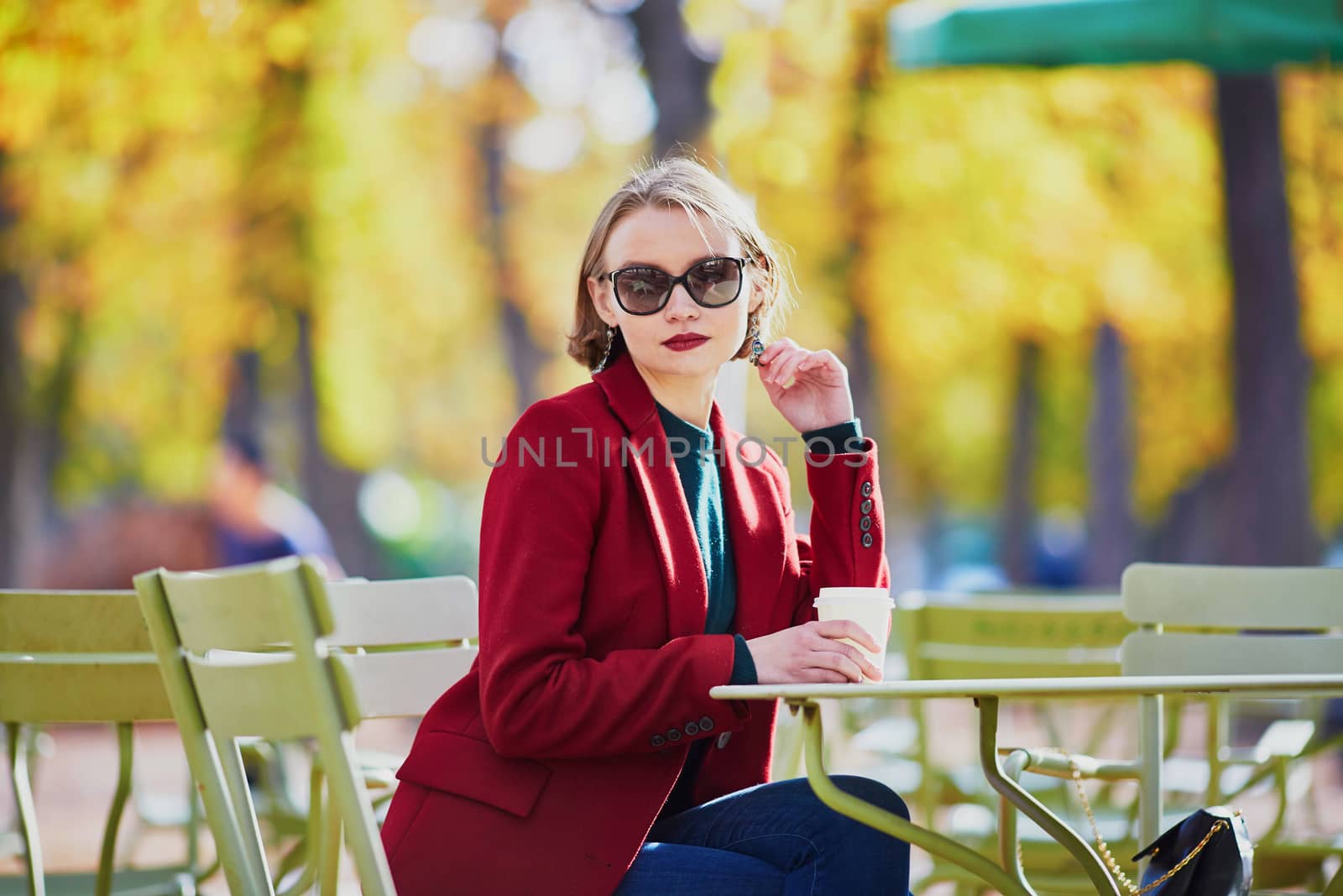 Elegant Parisian woman drinking coffee in park on a bright sunny autumn day
