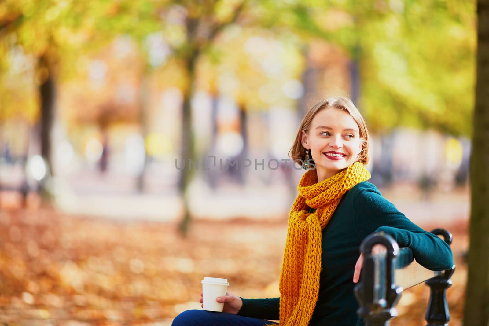 Happy young girl in yellow scarf with coffee to go walking in autumn park on a bright fall day
