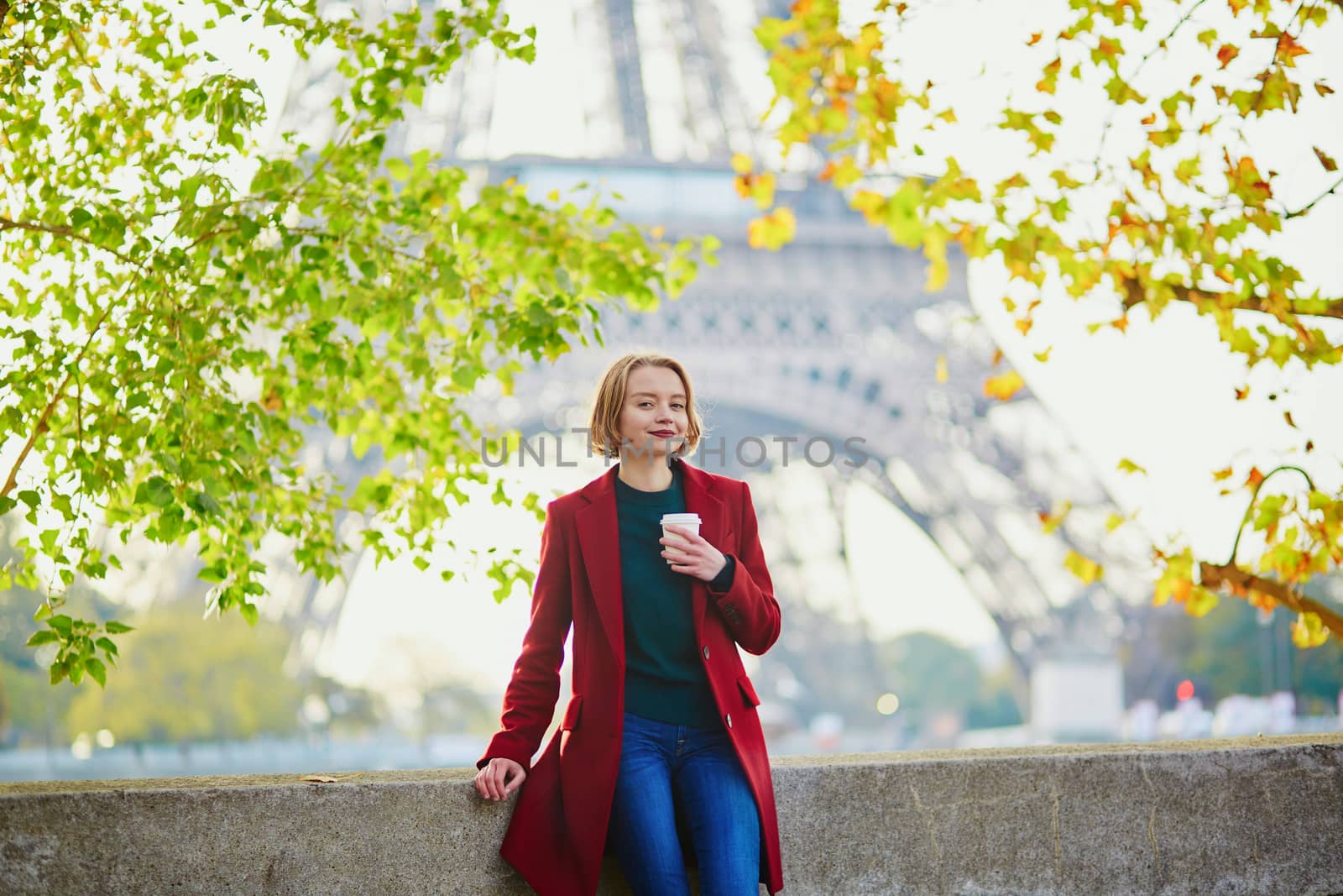 Beautiful young French woman drinking coffee near the Eiffel tower in Paris on a fall or spring day