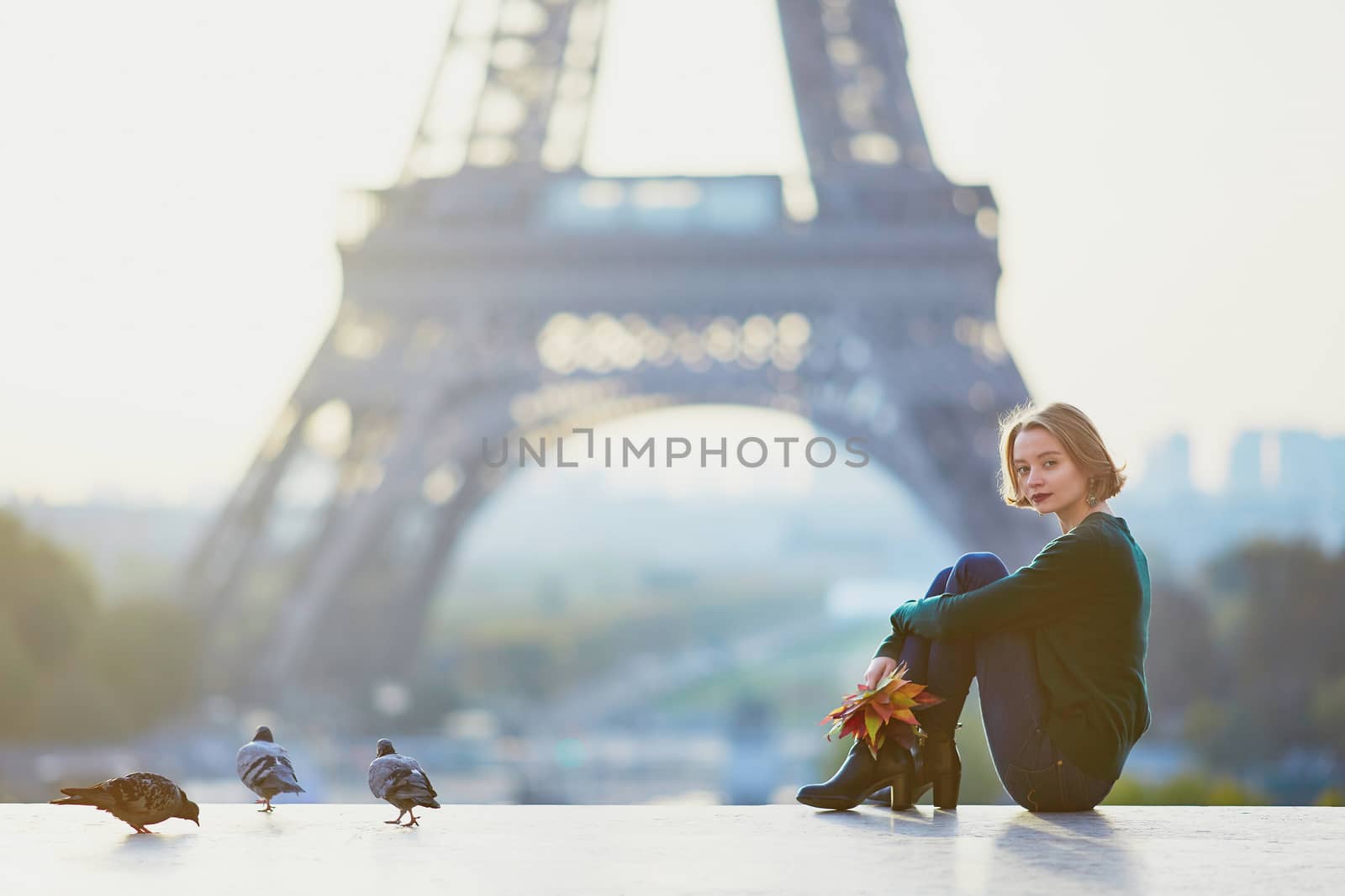 Beautiful young French woman with bunch of colorful autumn leaves near the Eiffel tower in Paris on a fall day