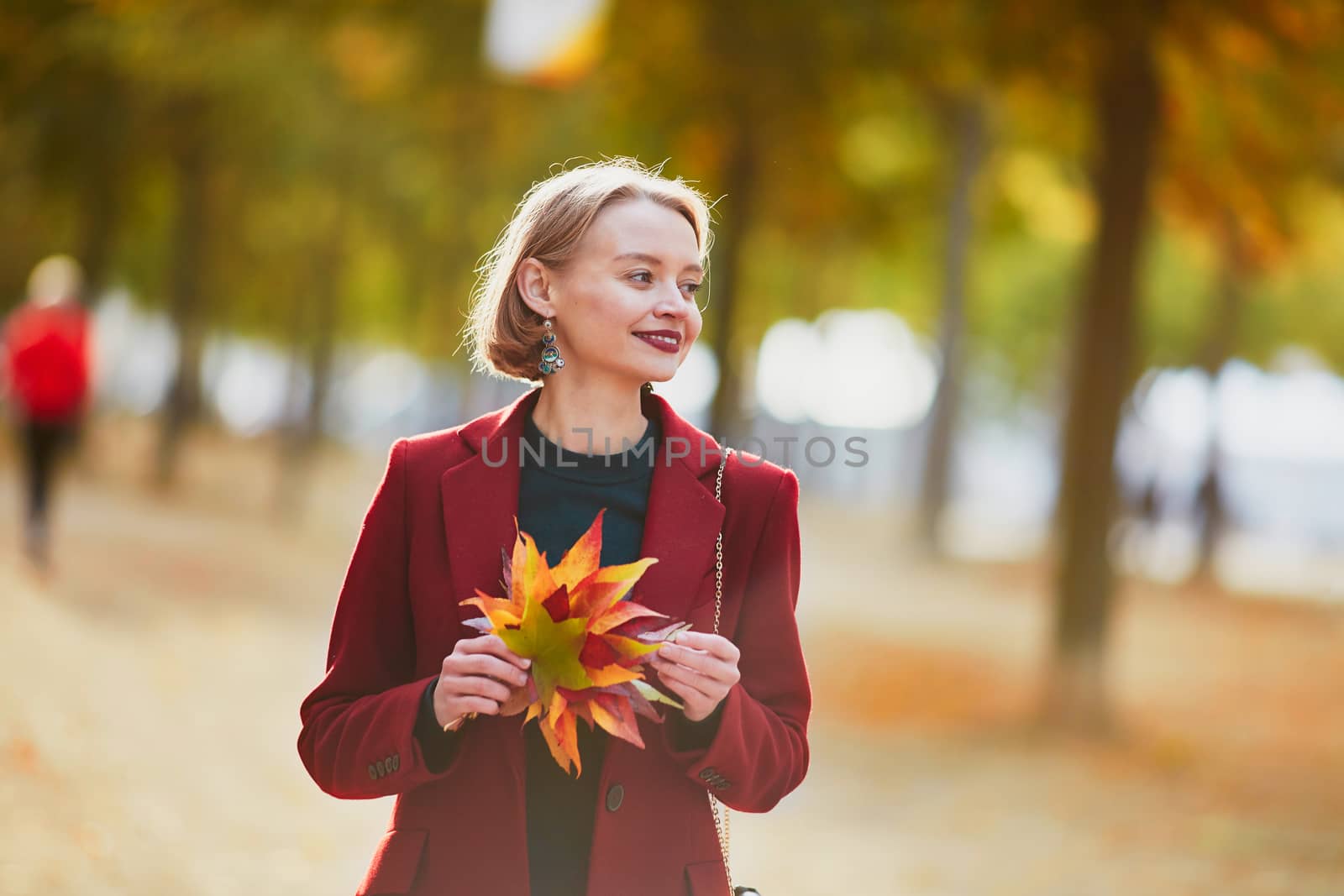 Beautiful young woman with bunch of colorful autumn leaves walking in park on a fall day