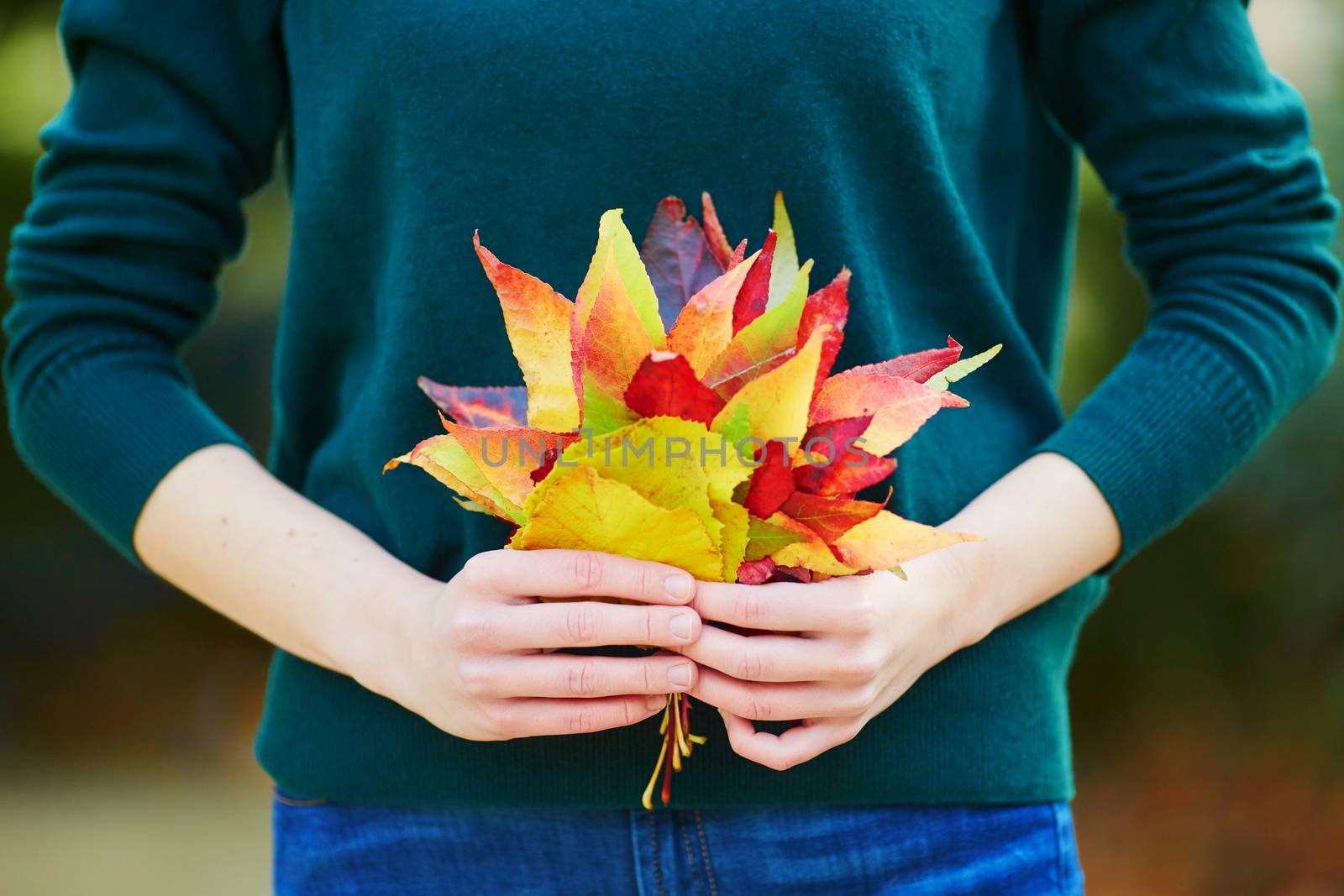 Beautiful young woman with bunch of colorful autumn leaves walking in park on a fall day. Luxembourg garden, Paris, France