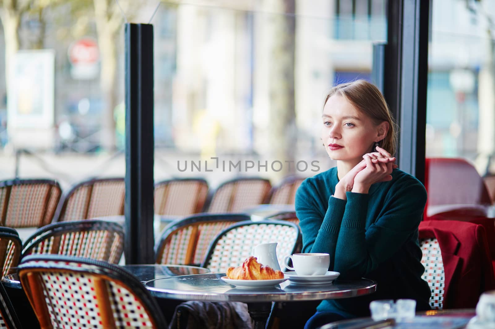 Elegant French woman drinking coffee in Parisian cafe near the window
