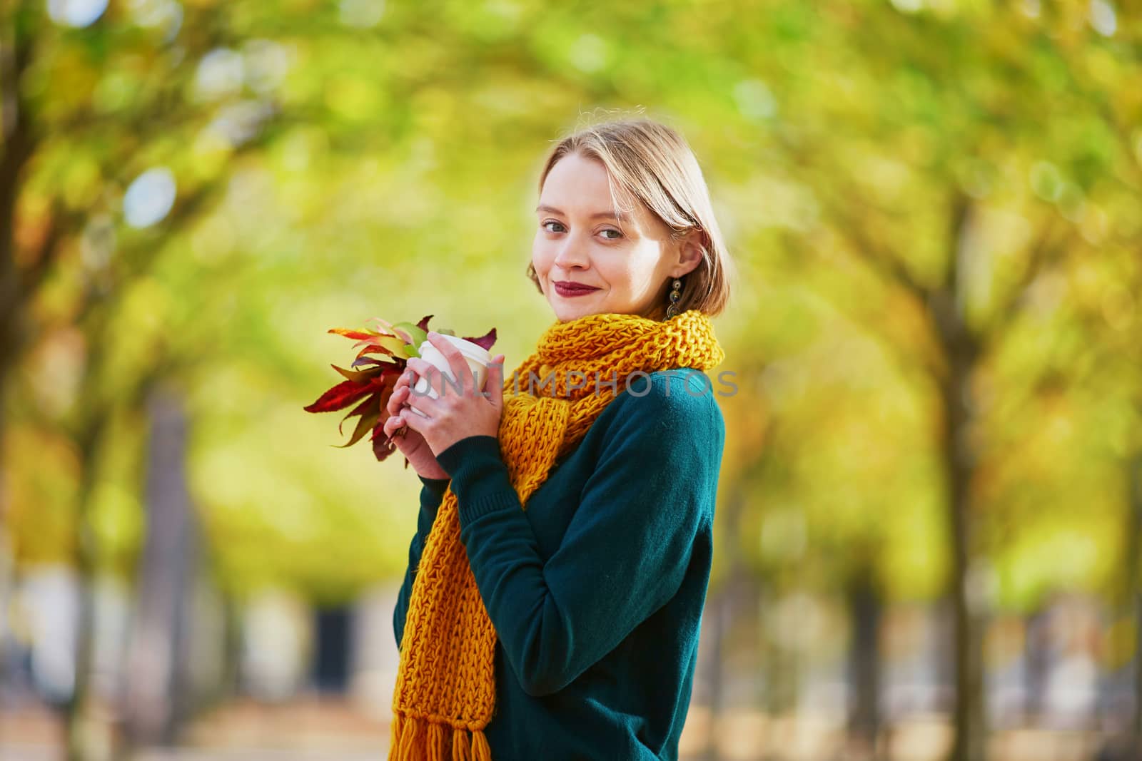 Happy young girl in yellow scarf with coffee to go walking in autumn park on a bright fall day