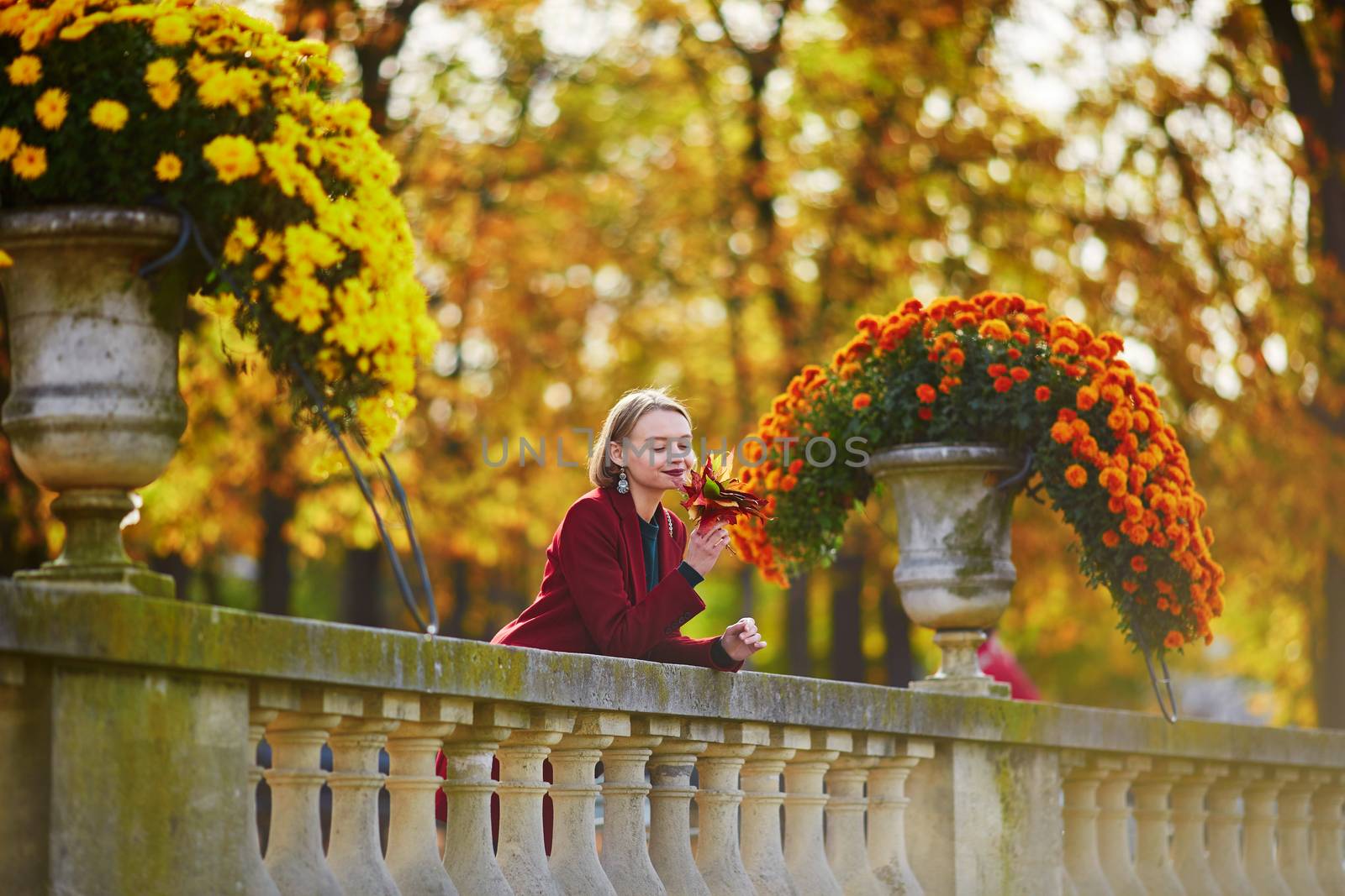 Beautiful young woman with bunch of colorful autumn leaves walking in park on a fall day. Luxembourg garden, Paris, France