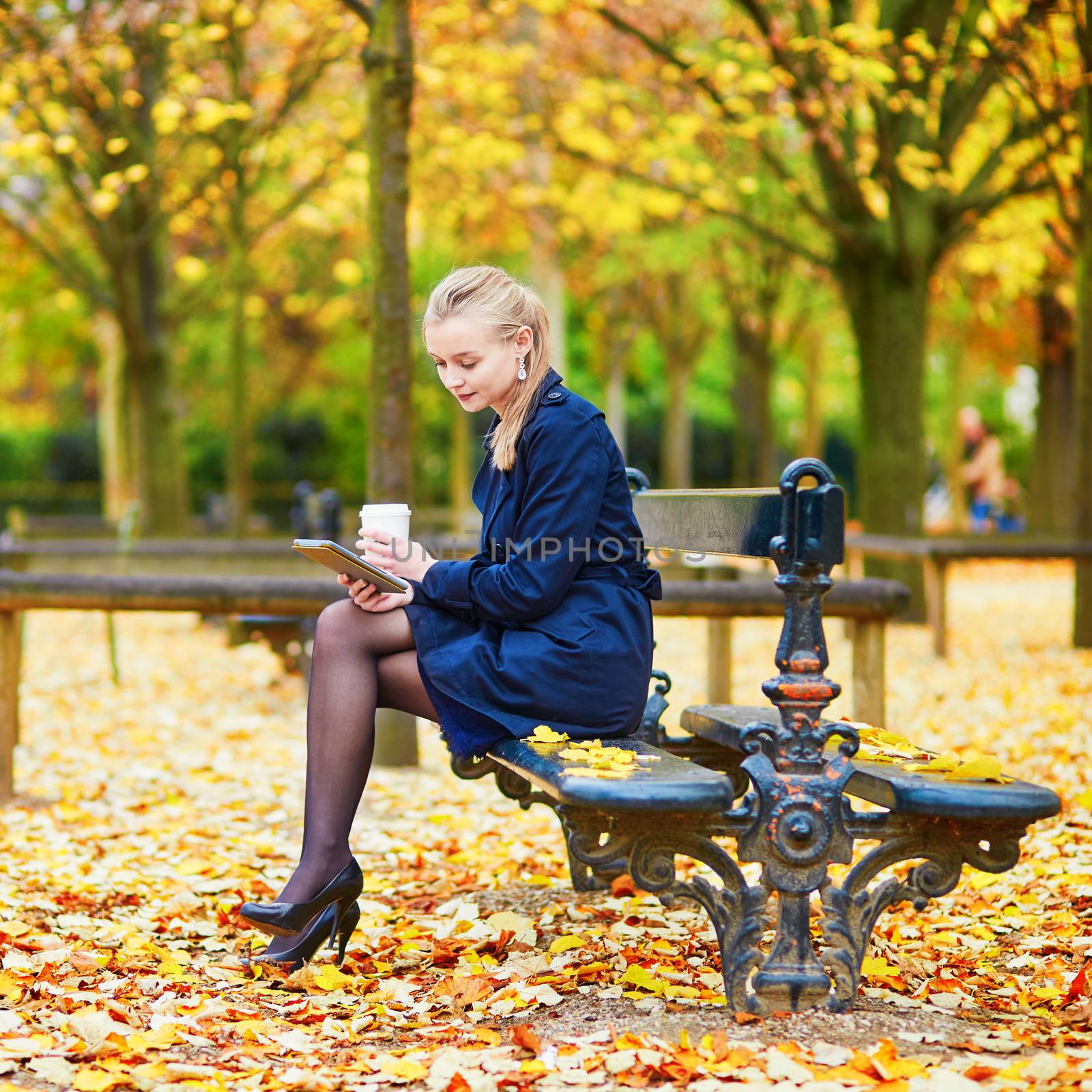 Beautiful young woman in the Luxembourg garden of Paris on a fall day, drinking coffee to go