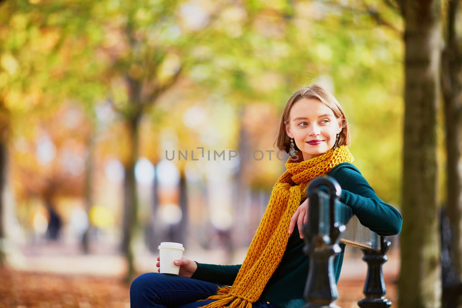 Happy young girl in yellow scarf with coffee to go walking in autumn park on a bright fall day