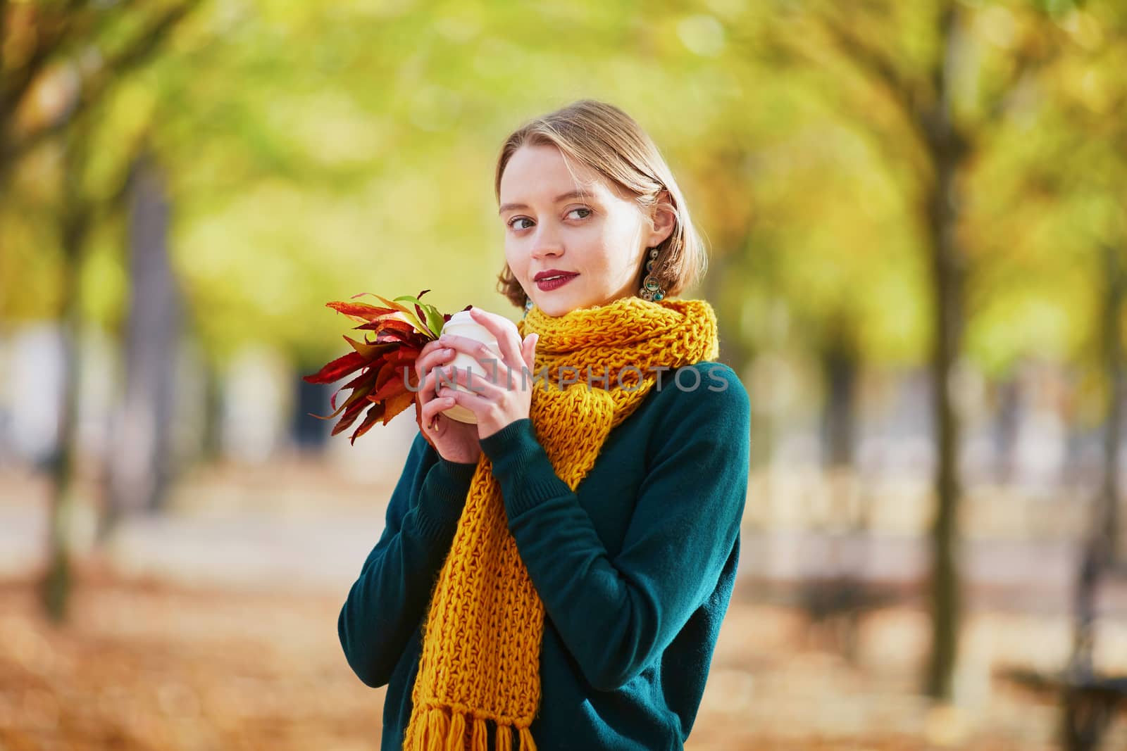 Happy young girl in yellow scarf with coffee to go walking in autumn park on a bright fall day