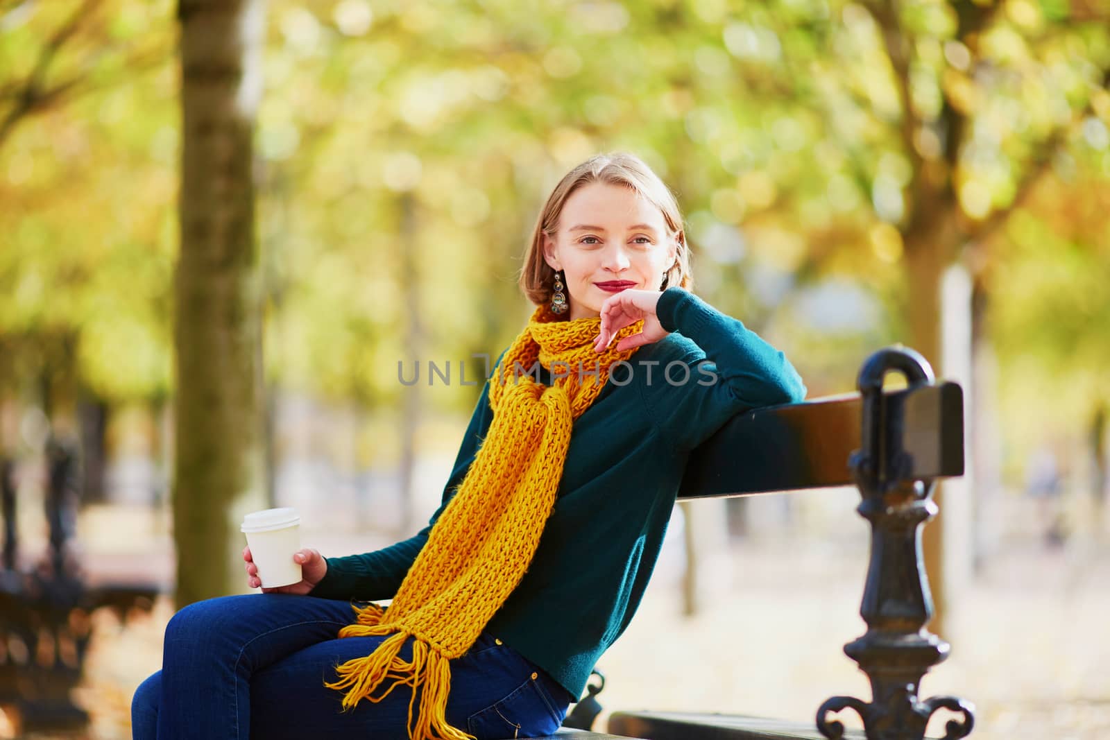 Happy young girl in yellow scarf with coffee to go walking in autumn park on a bright fall day