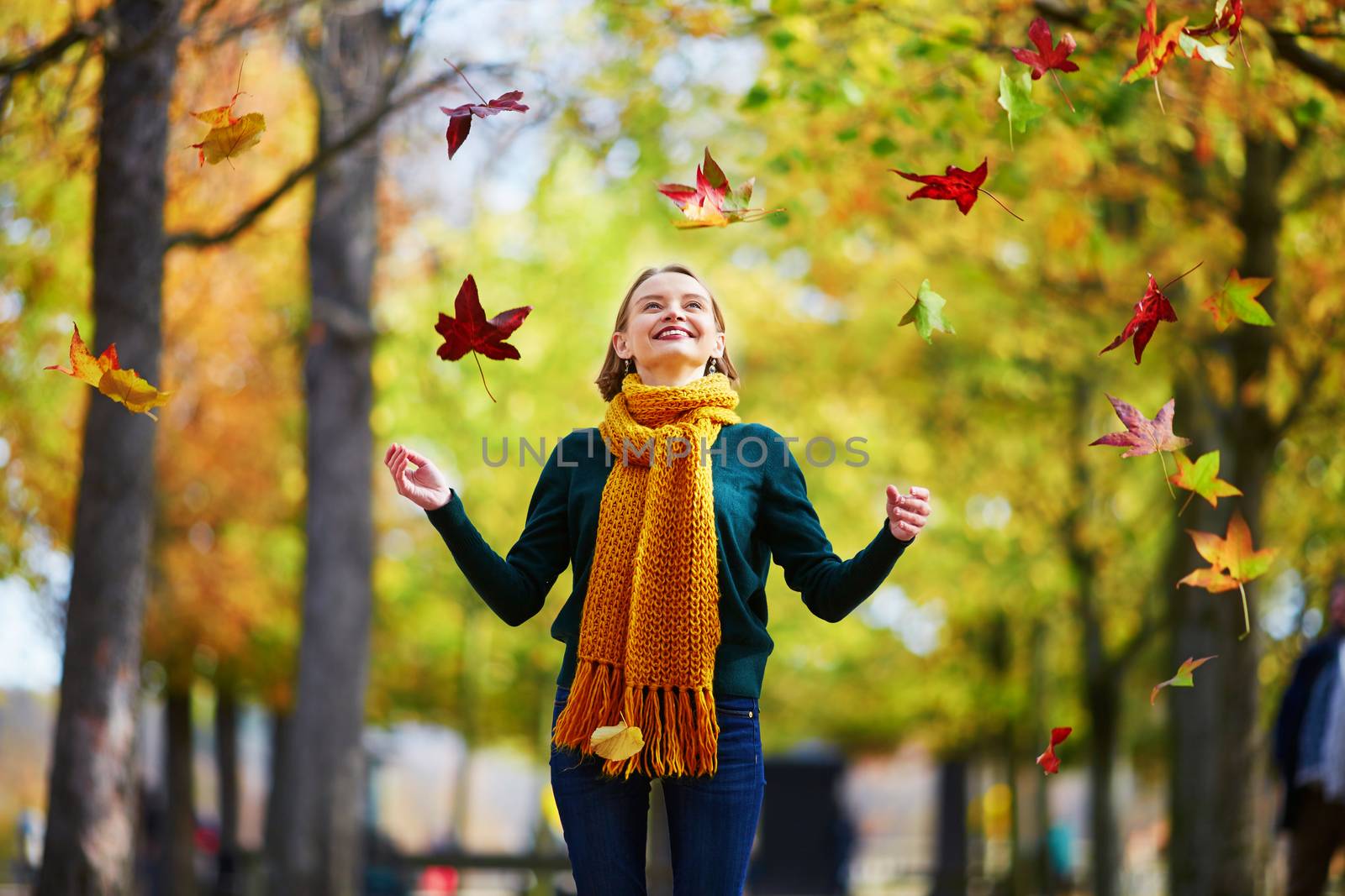 Beautiful young woman with htrowing colorful autumn leaves while walking in park on a fall day. Luxembourg garden, Paris, France