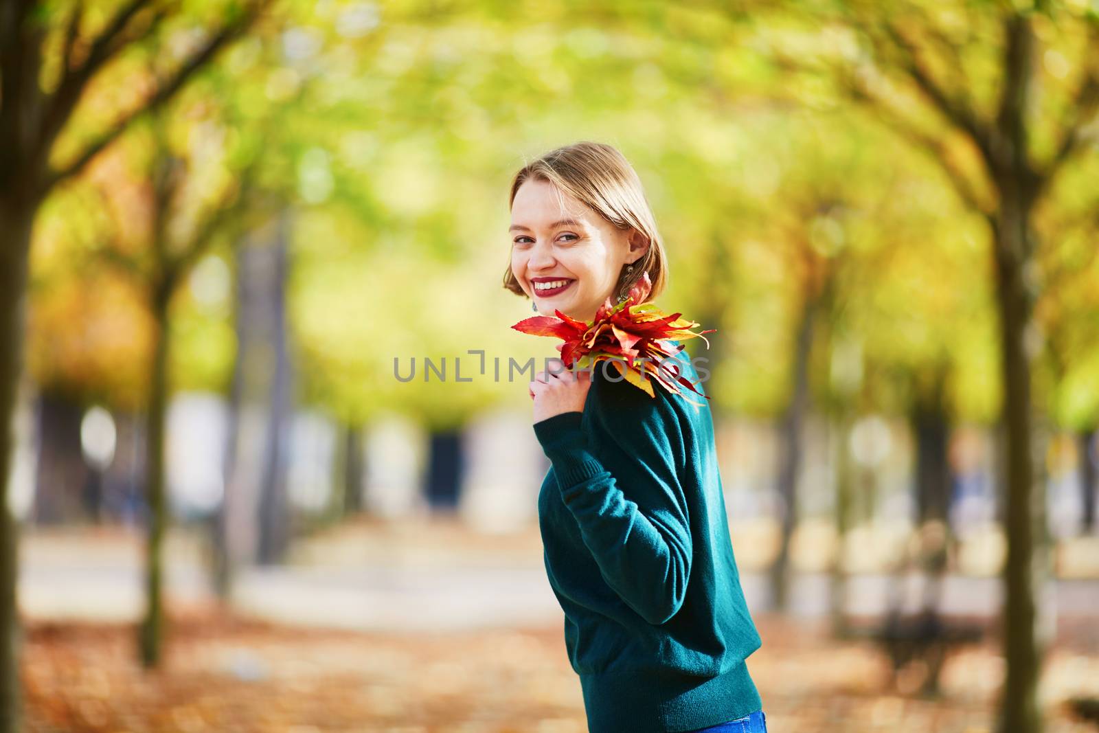 Beautiful young woman with bunch of colorful autumn leaves walking in park on a fall day. Luxembourg garden, Paris, France