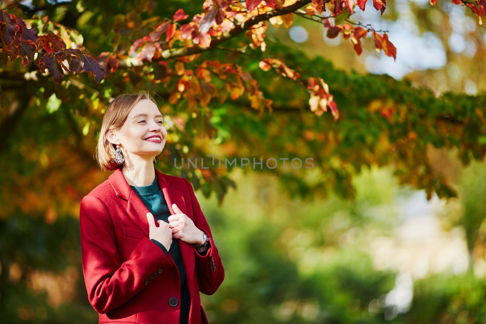 Beautiful young woman with bunch of colorful autumn leaves walking in park on a fall day. Luxembourg garden, Paris, France