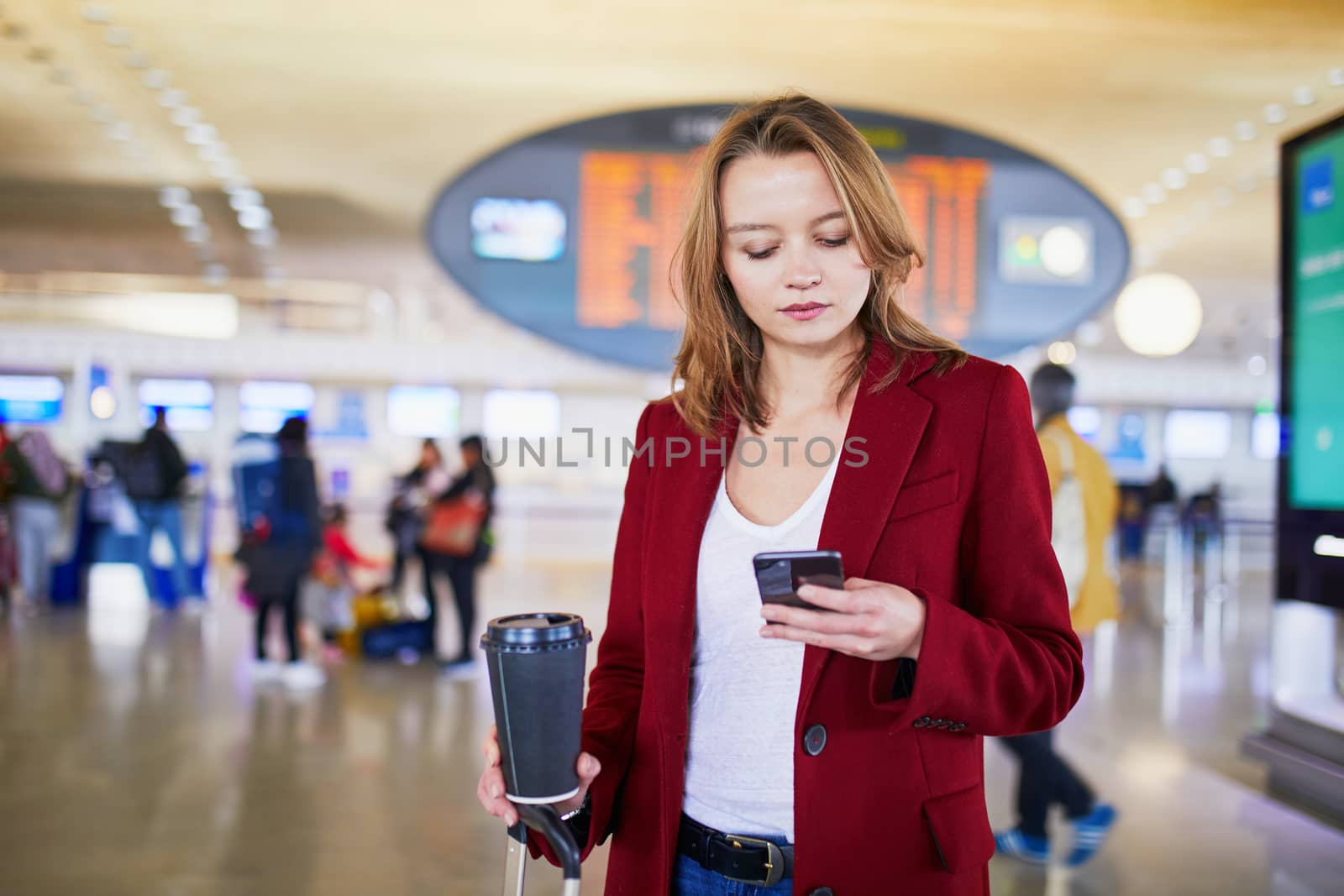 Young woman in international airport with luggage and coffee to go waiting for her flight