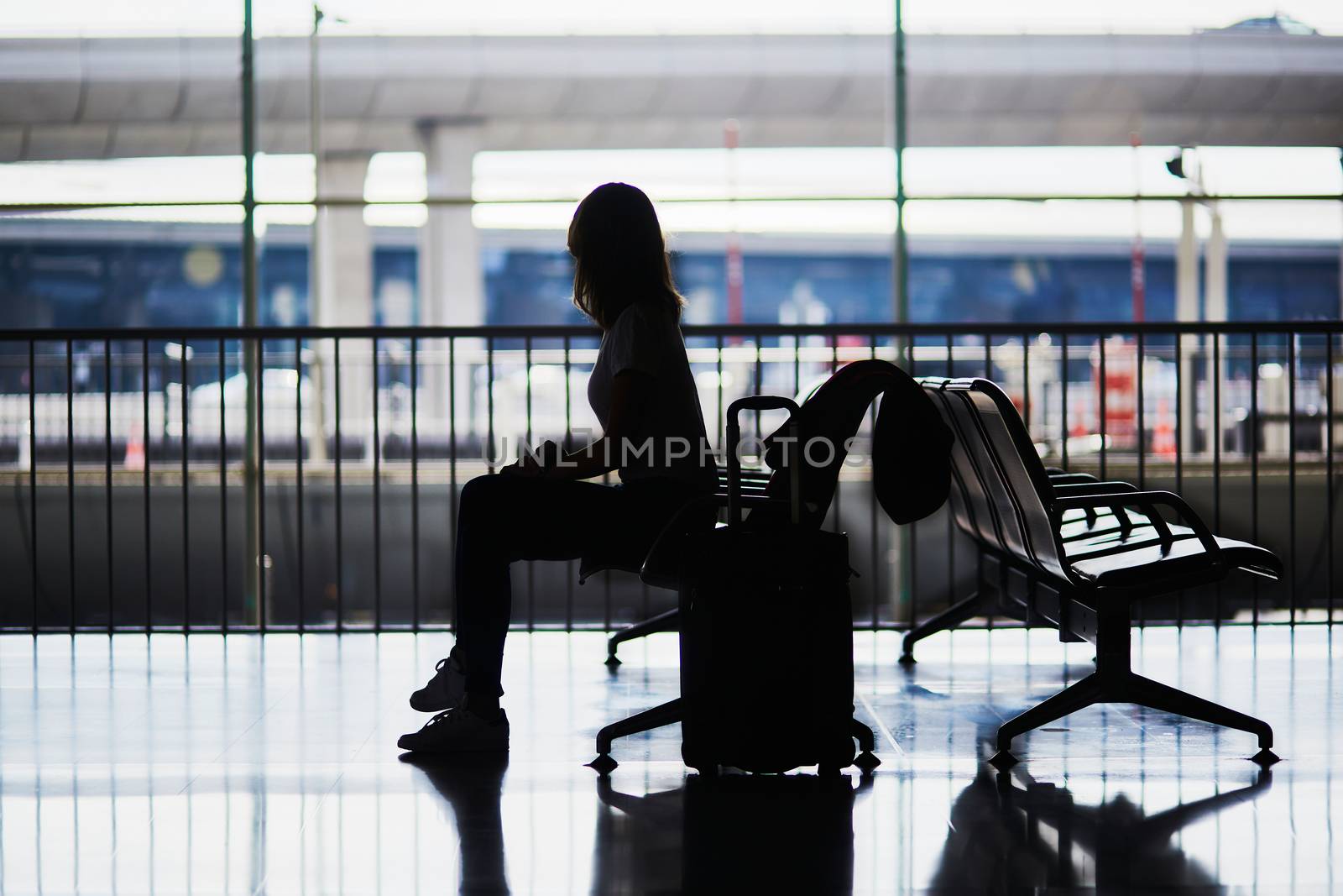 Silhouette of young woman in international airport sitting and waiting for her flight.