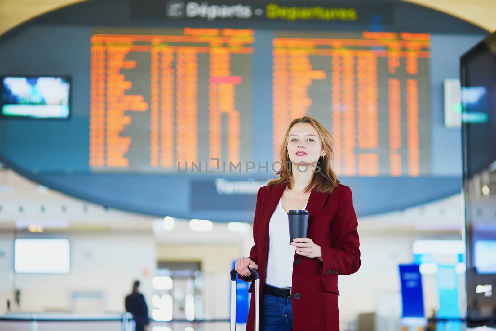 Young woman in international airport with luggage and coffee to go waiting for her flight