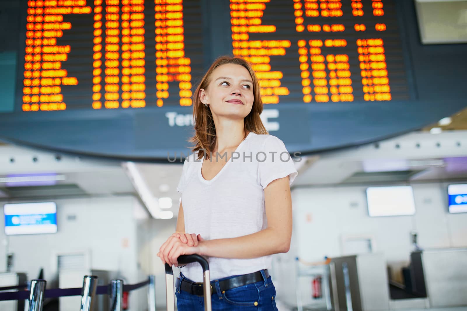 Young woman in international airport with luggage near information board waiting for her flight