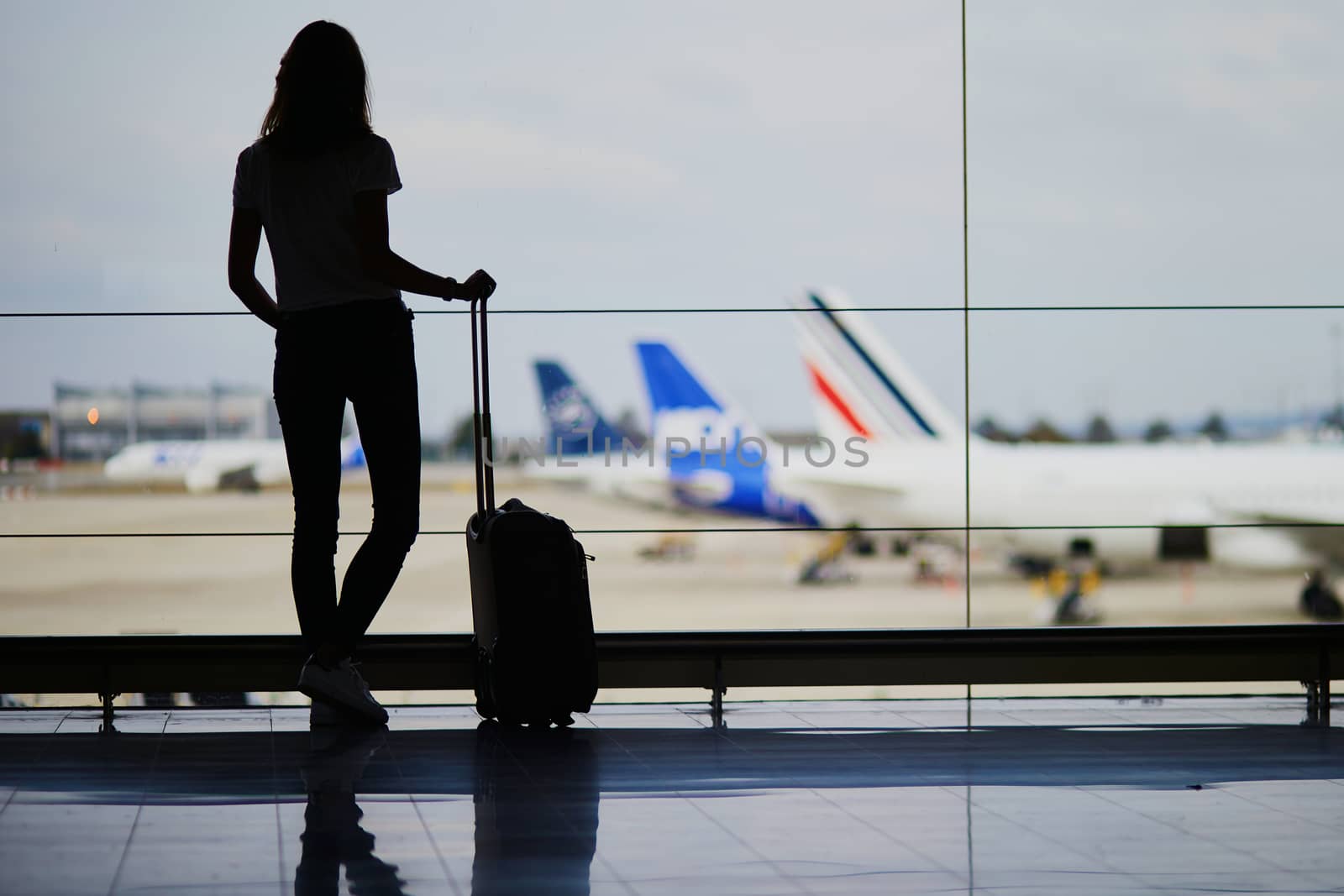 Silhouette of young woman in international airport, looking through the window at planes