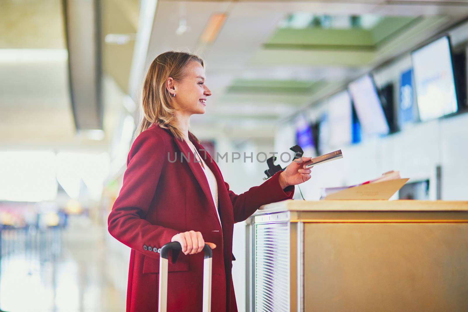 Young woman in international airport at check-in counter giving her passport to officer