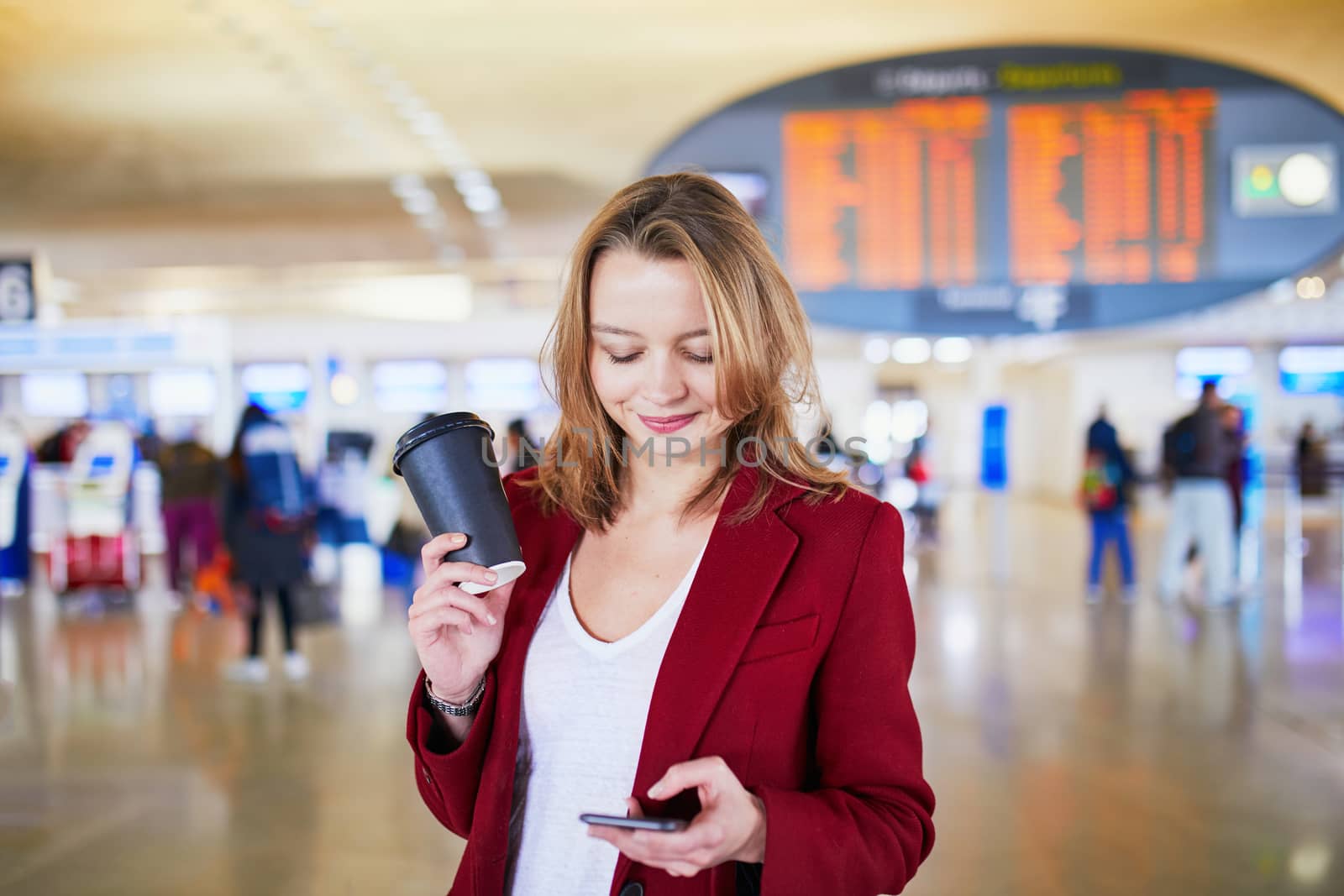 Young woman in international airport with luggage and coffee to go waiting for her flight