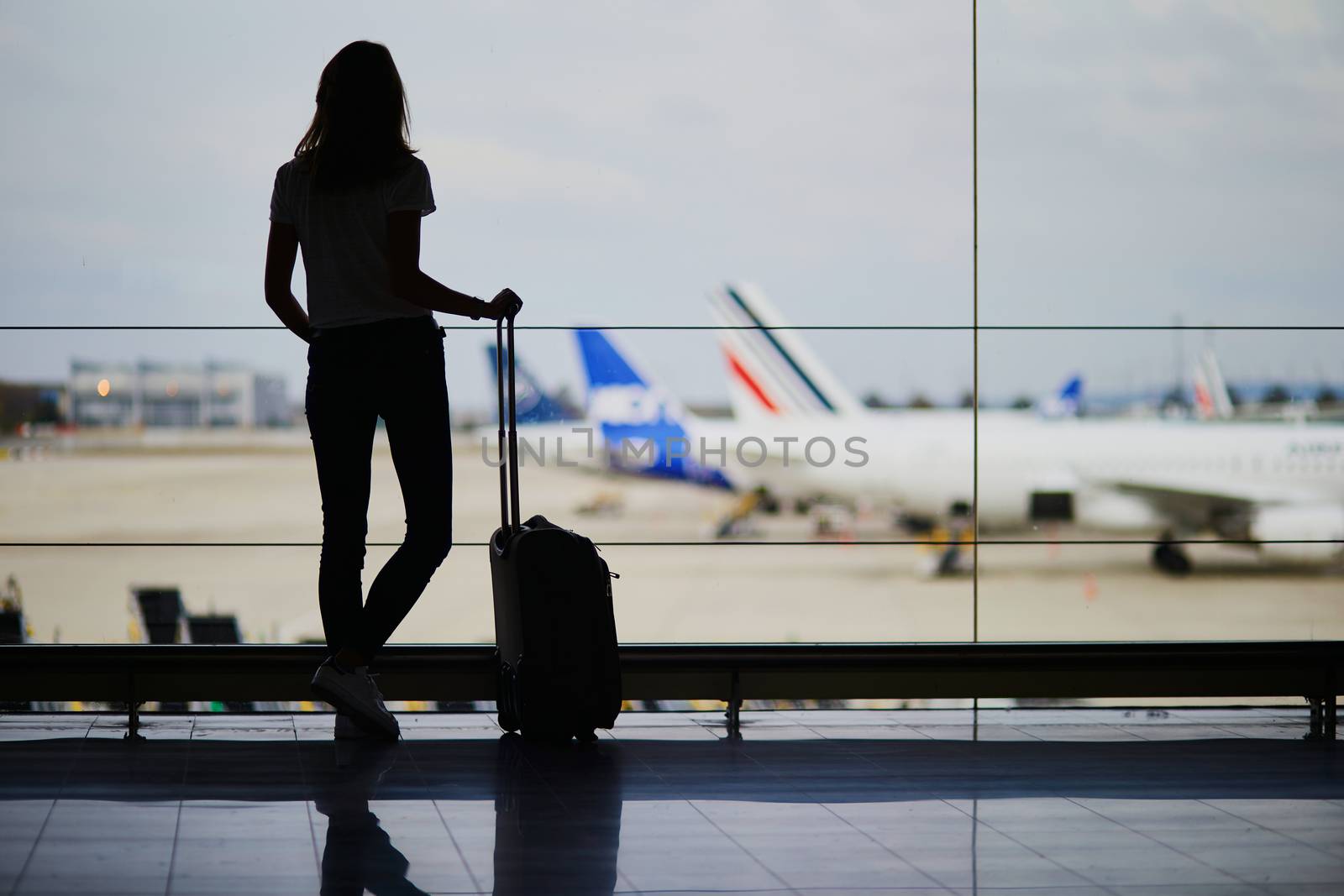 Silhouette of young woman in international airport, looking through the window at planes