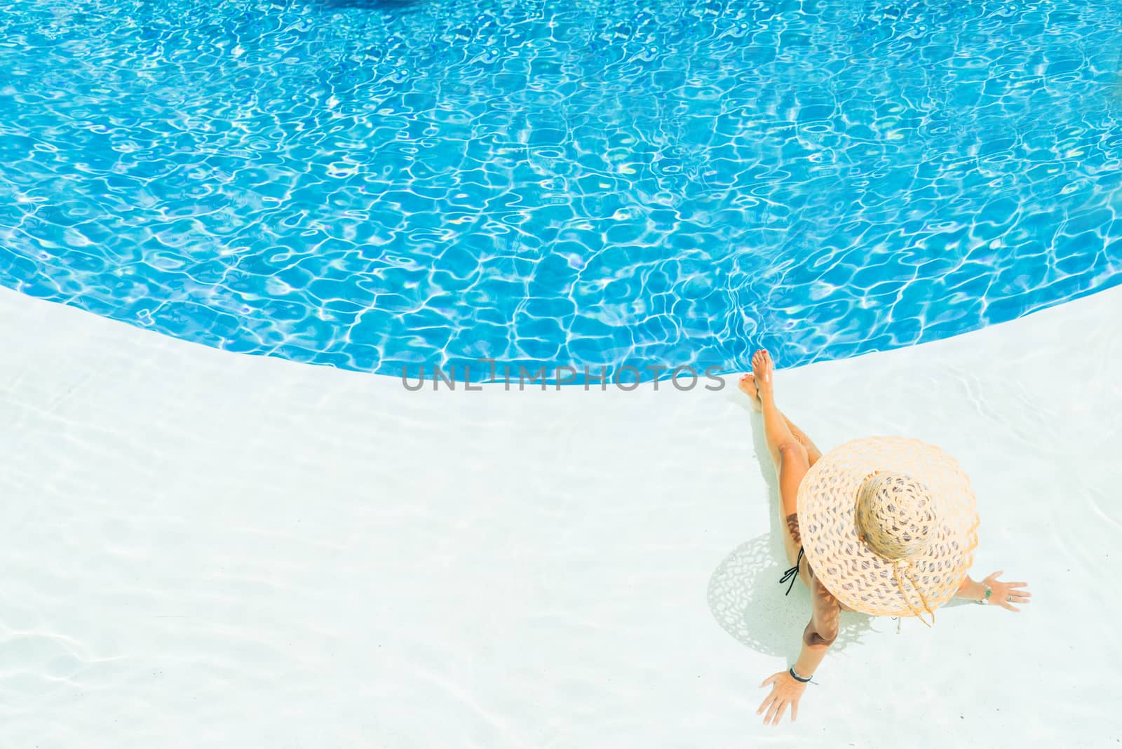 beautiful woman in a hat sitting on the edge of the swimming pool