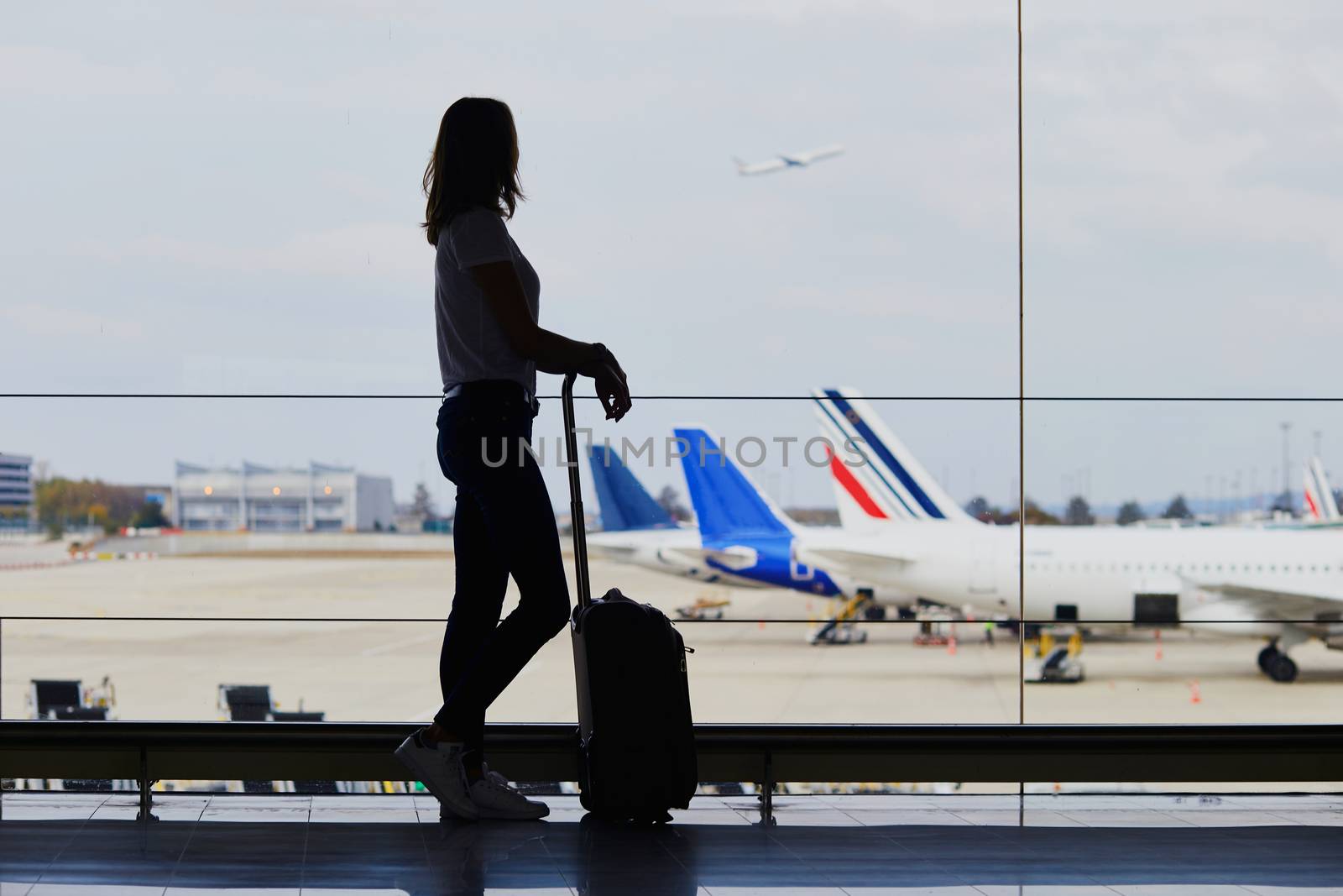 Young woman in international airport, looking through the window at planes