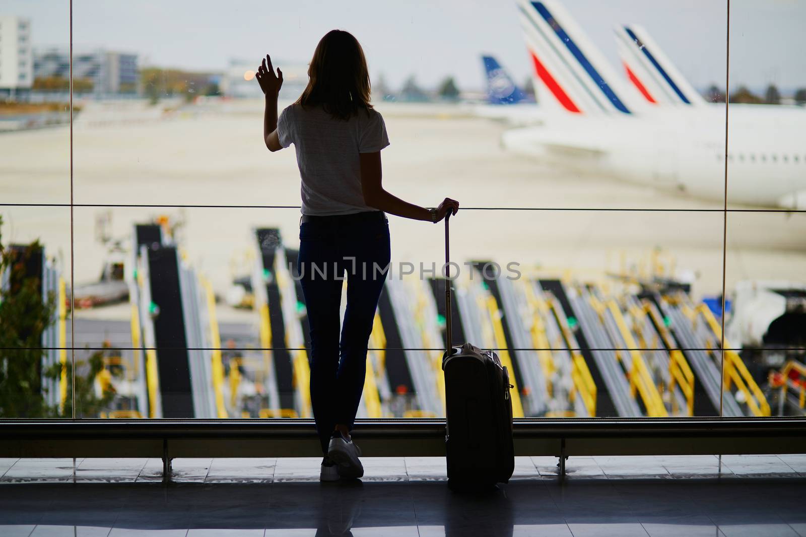 Young woman in international airport, looking through the window at planes