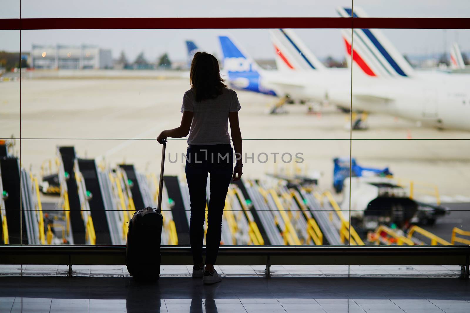 Silhouette of young woman in international airport, looking through the window at planes