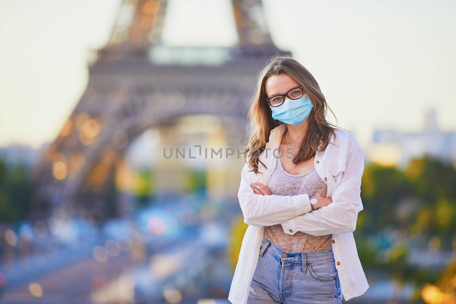 Young girl standing near the Eiffel tower in Paris and wearing protective face mask by jaspe