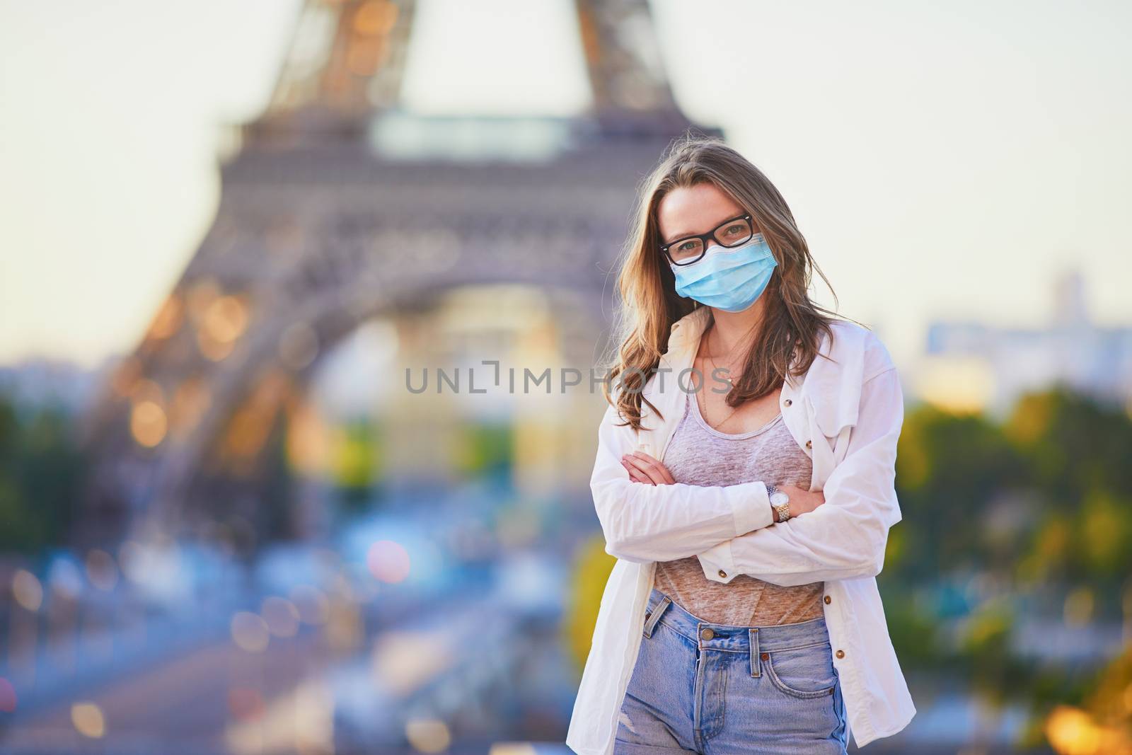 Young girl standing near the Eiffel tower in Paris and wearing protective face mask during coronavirus outbreak. Pandemic and lockdown in France. Tourist spending vacation in France after quarantine