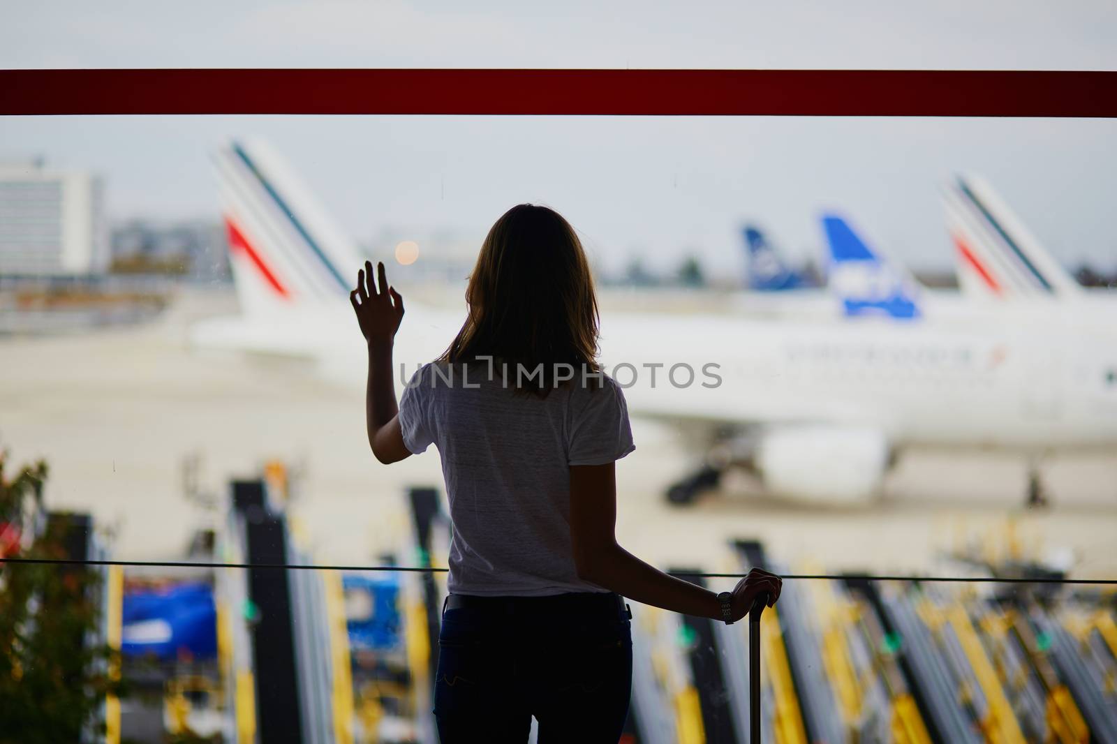 Silhouette of young woman in international airport, looking through the window at planes