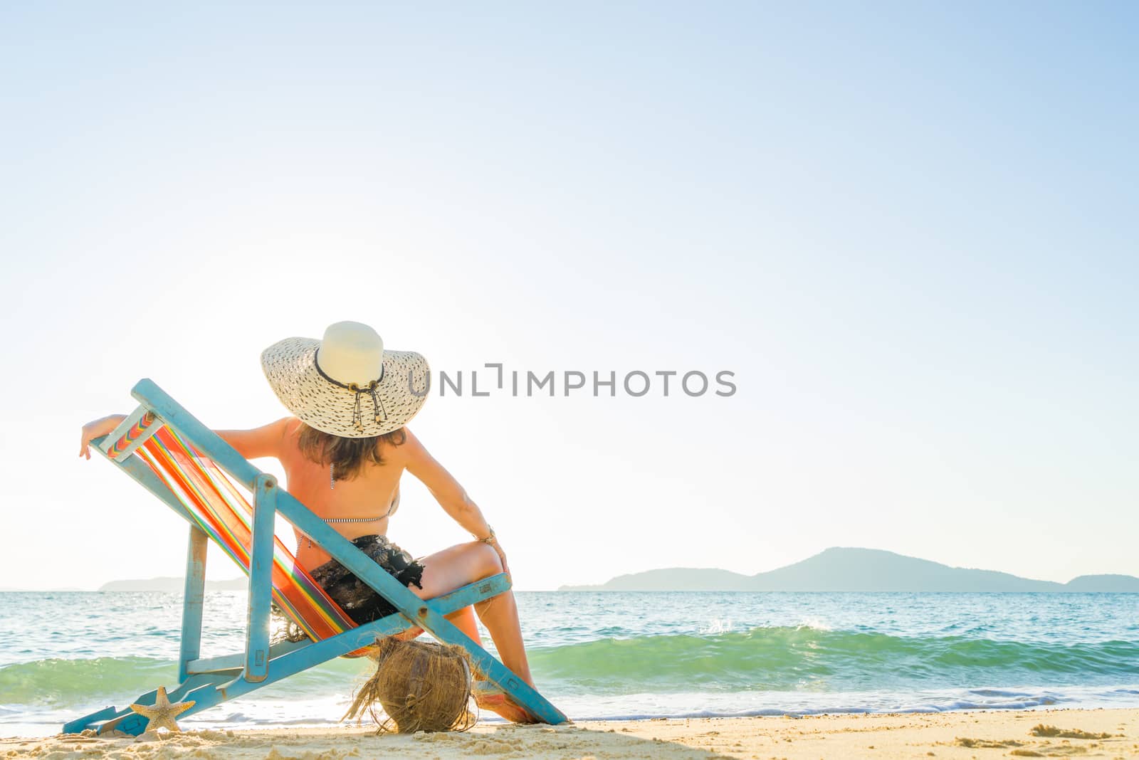Young woman in hat sitting on beach by Netfalls