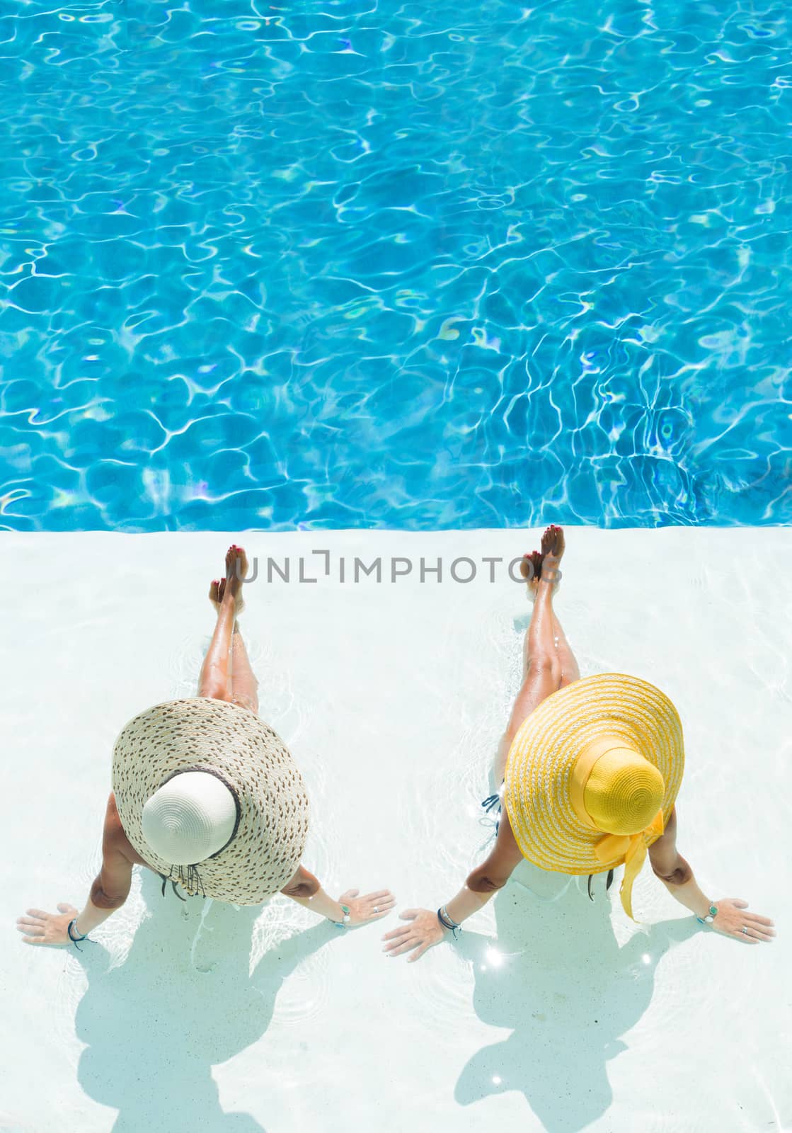 Two women in a hat sitting on the edge of the swimming pool