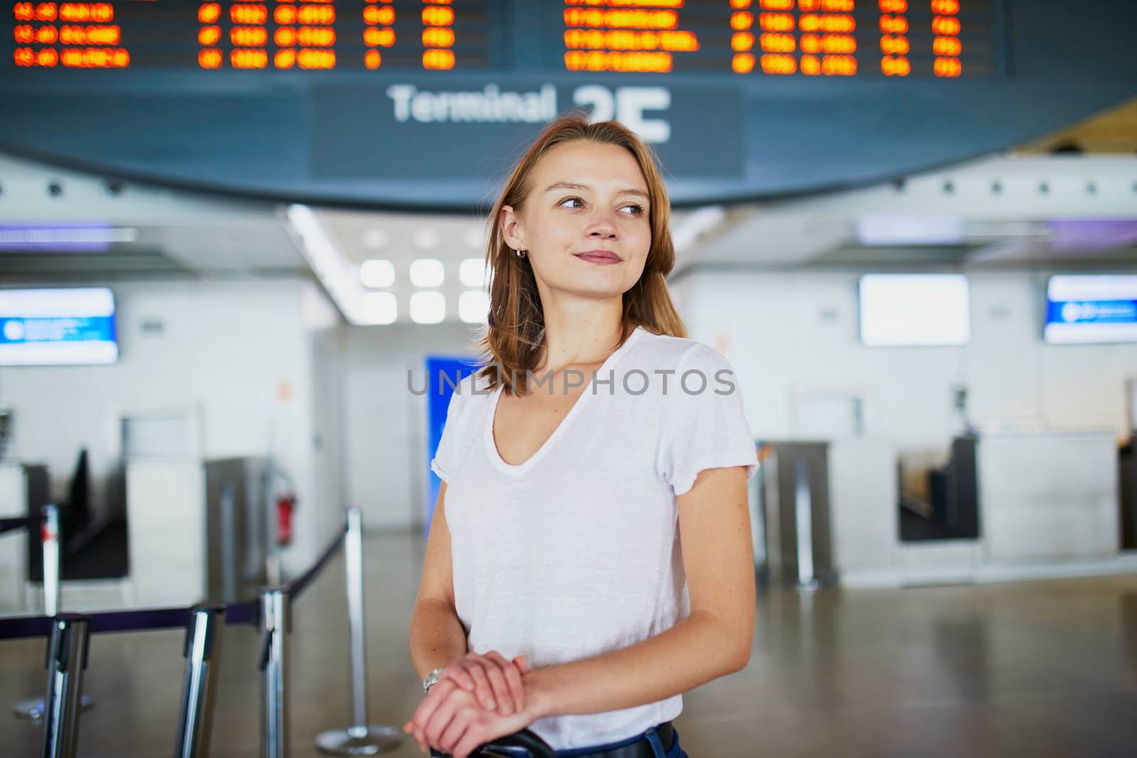 Young woman in international airport with luggage near information board waiting for her flight