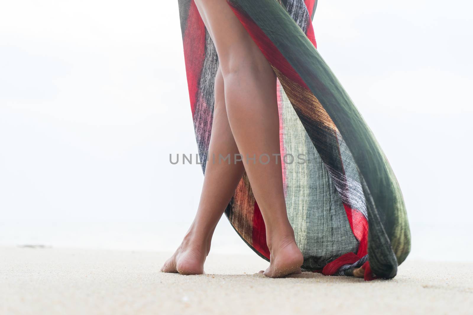 Standing woman legs posing on the beach wearing a pareo 
