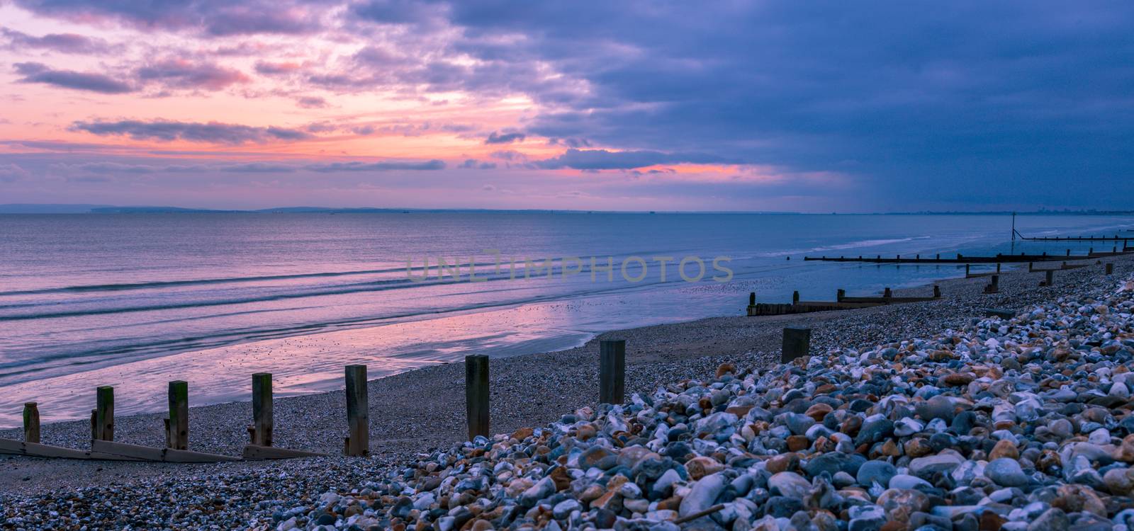 Sunset, groynes and silhouettes on the East Wittering shoreline, England, UK.