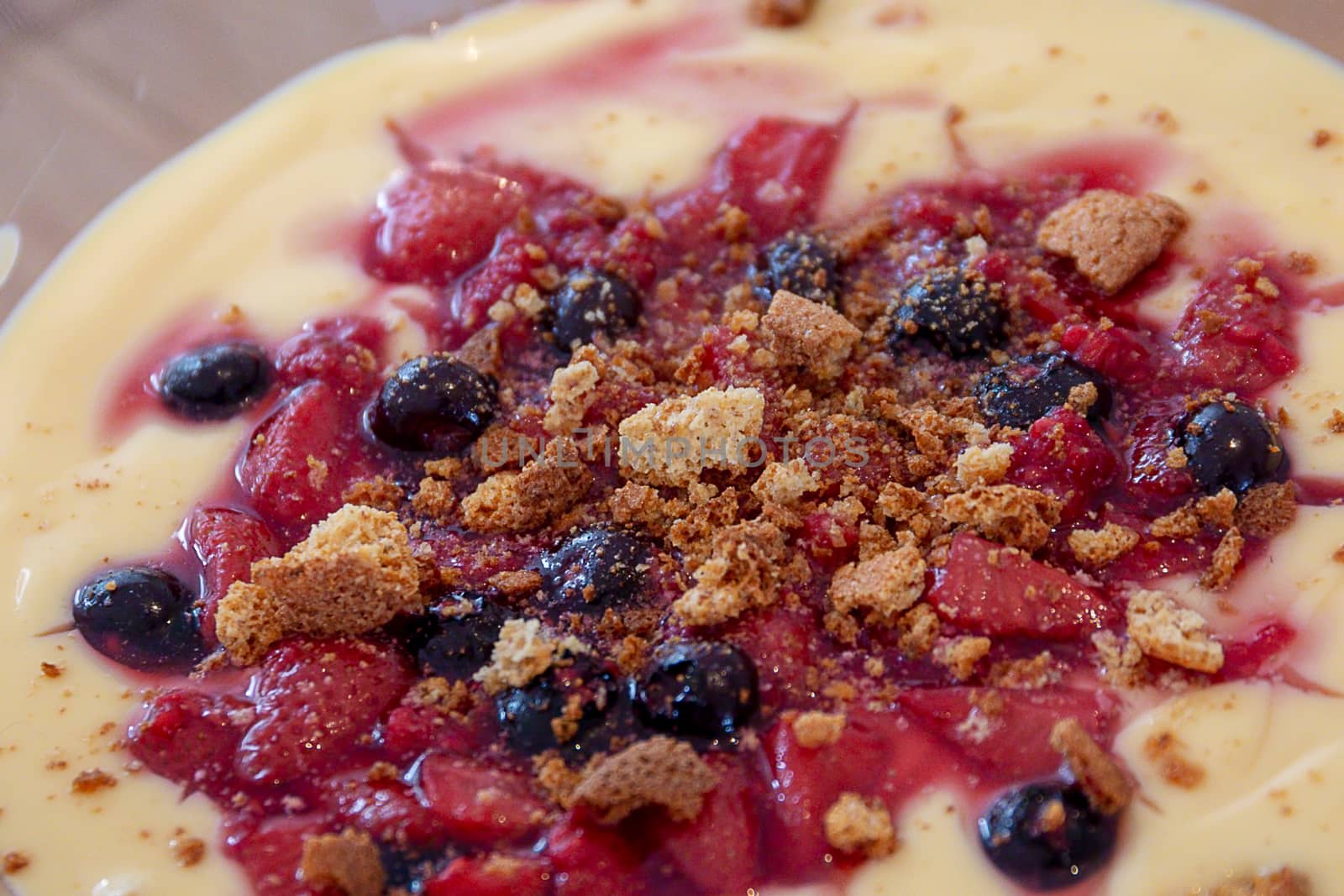 Homemade trifle with custard, strawberries, blueberries and crumbled biscuits