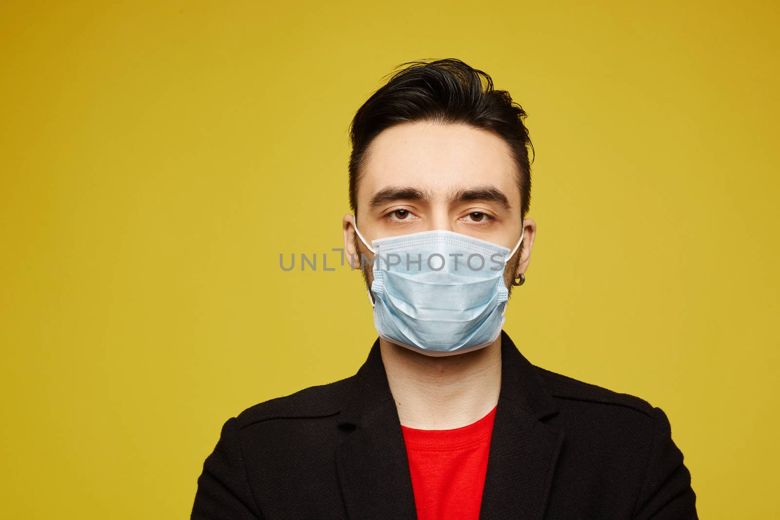 Portrait of handsome young man in black protective mask looking in camera, isolated on yellow background. Seasonal illness and seasonal flu prevention. Young man wearing a protective mask to prevent infection and airborne respiratory illness