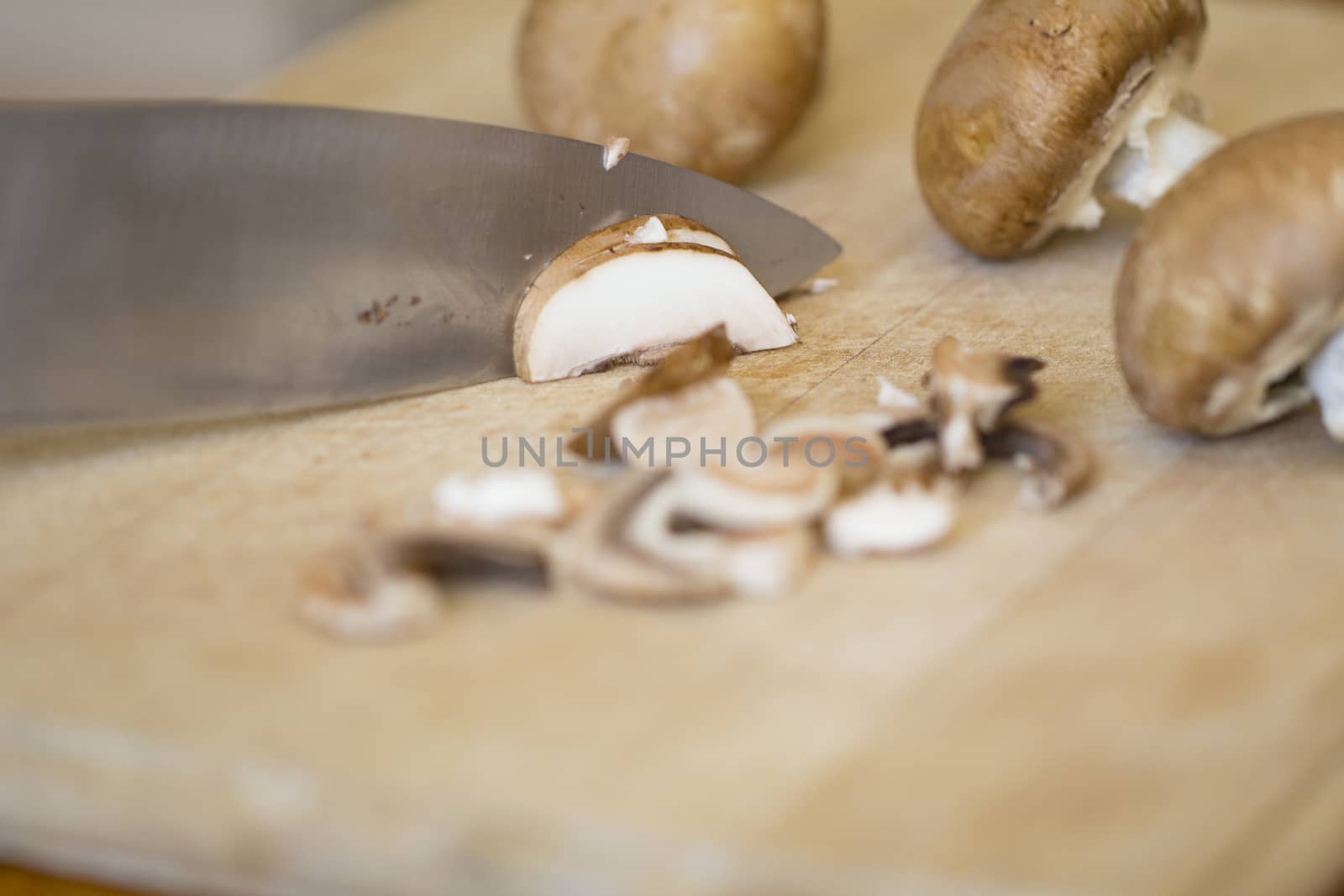 Chopping Cremini mushrooms, agaricus risporus on a wooden chopping board