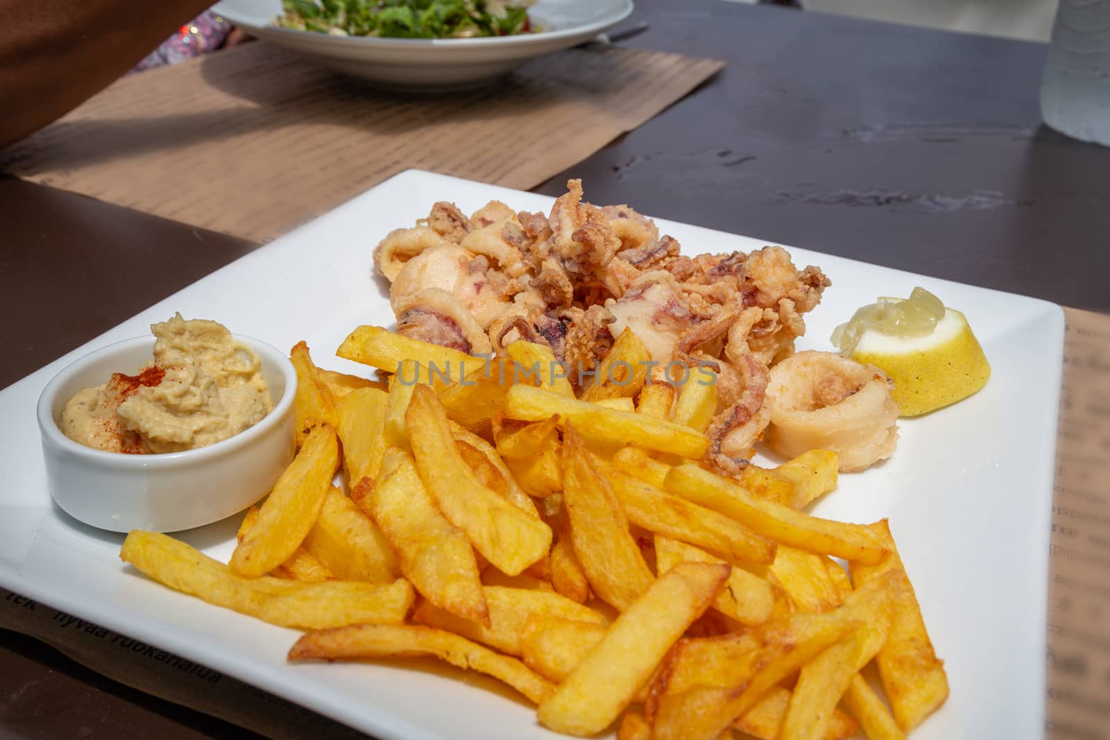 A plate of fried calamari and chips with s pot of hummus