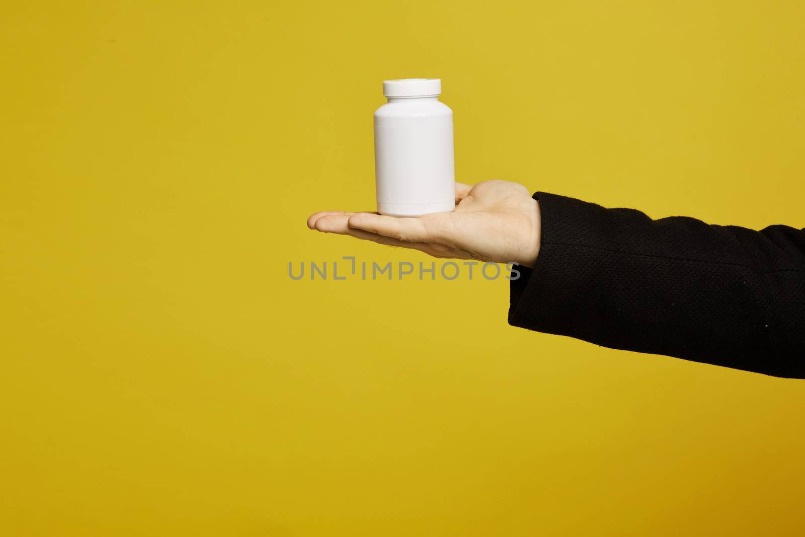 A white bottle of drugs on a male palm on yellow background, isolated with copy space. Healthcare concept. Prevention infection, viruses and seasonal illness. COVID-19