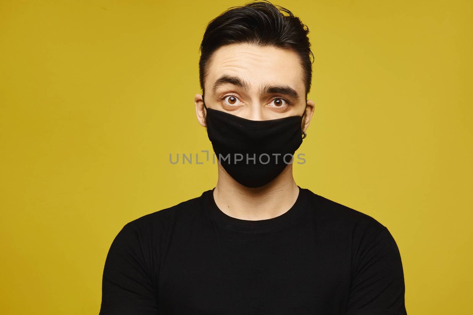 Handsome man in black t-shirt and black protective mask isolated on yellow background. Healthy lifestyle concept, seasonal illness, and seasonal flu concept. Young man wearing a protective mask to prevent infection and airborne respiratory illness