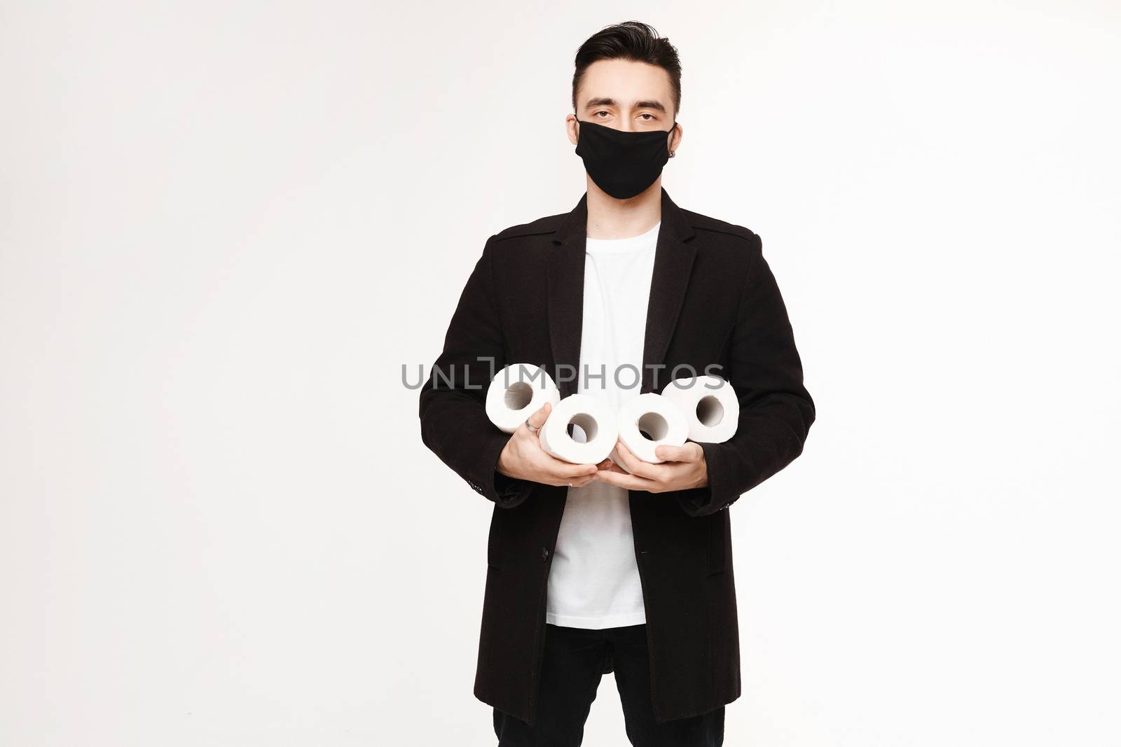 Handsome young man in black protective mask holding four rolls of toilet paper, isolated on the white background. Young men in protective face mask keeps rolls of toilet paper.
