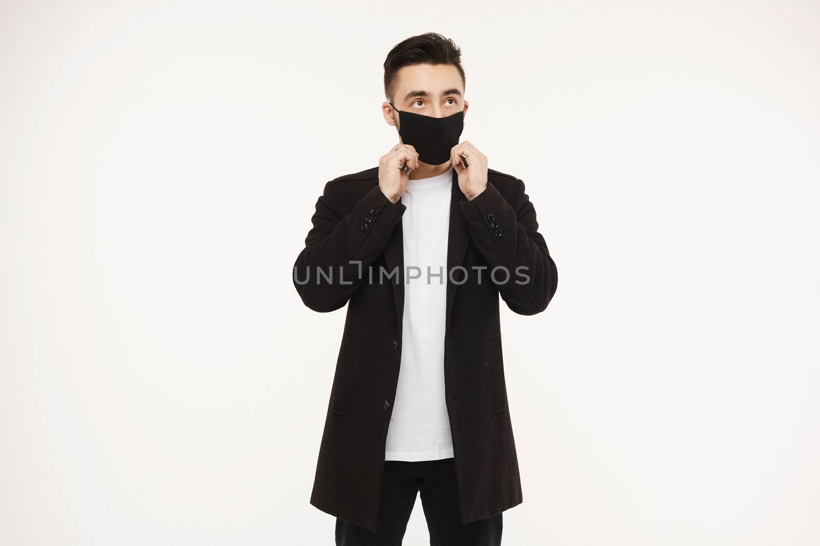 Handsome young man adjusting his black protective mask isolated on white background. Healthy lifestyle concept. Seasonal illness, and seasonal flu concept. Men wearing medical mask to prevent infection, airborne respiratory illness such as flu, 2019-nCoV.
