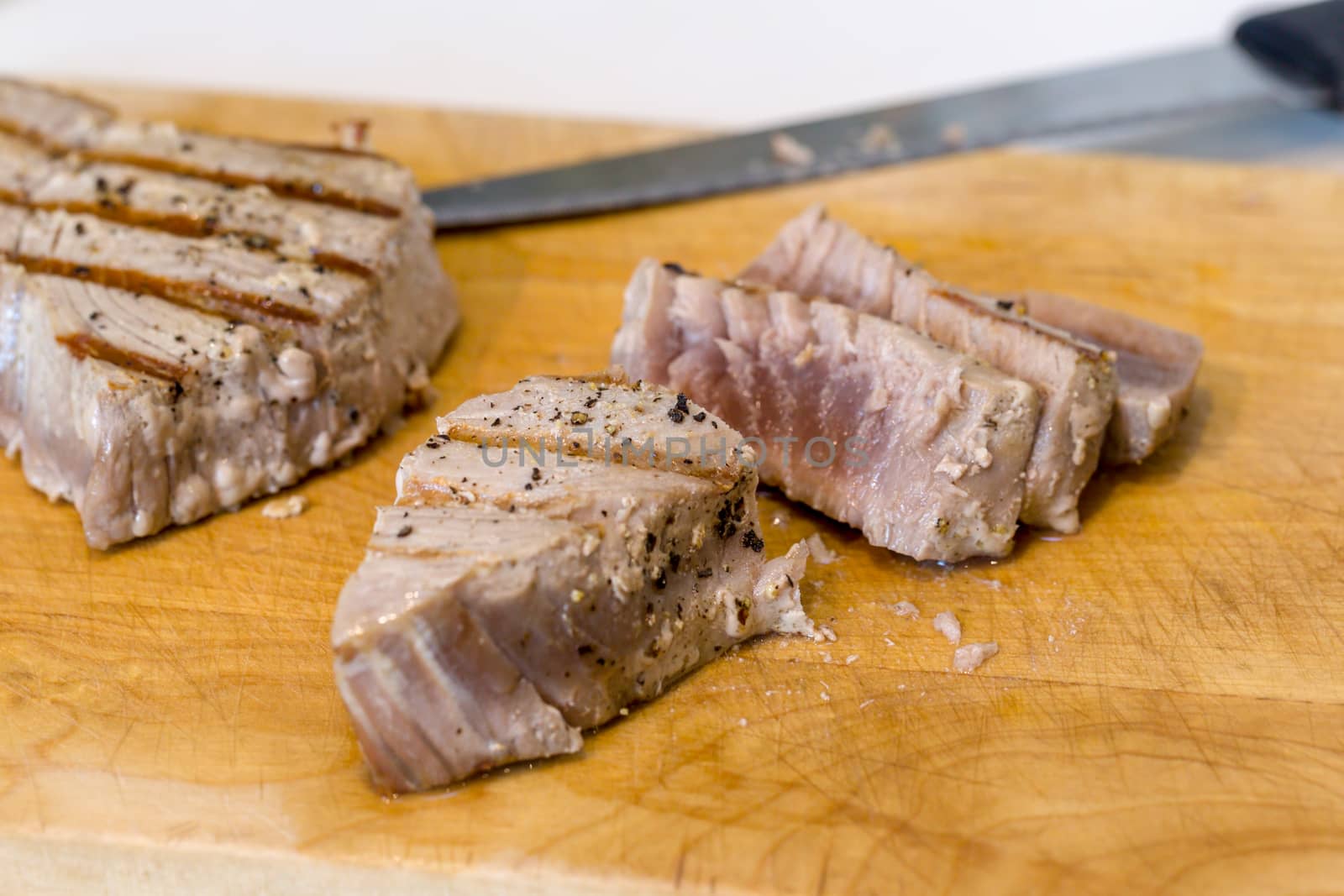 Chargrilled, seasoned tuna steaks cooked and sliced on a wooden chopping board