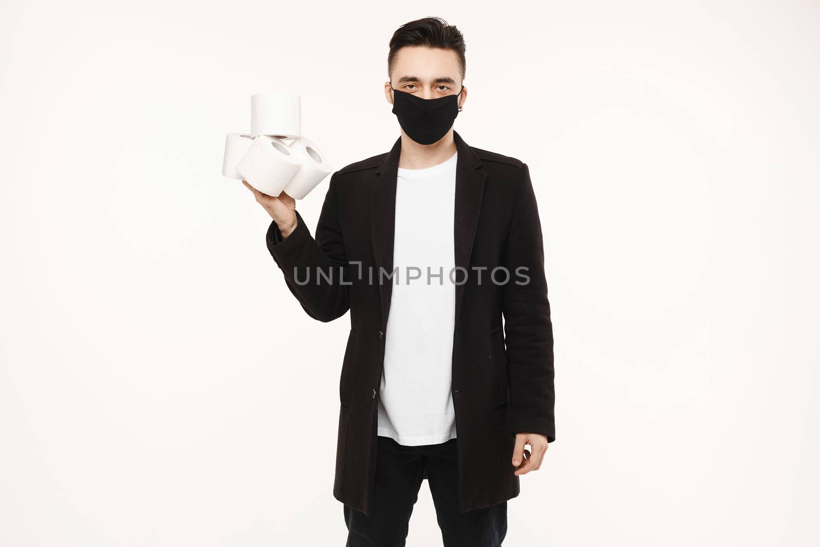Handsome young man in black protective mask holding four rolls of toilet paper, isolated on the white background. Young men in protective face mask keeps rolls of toilet paper.