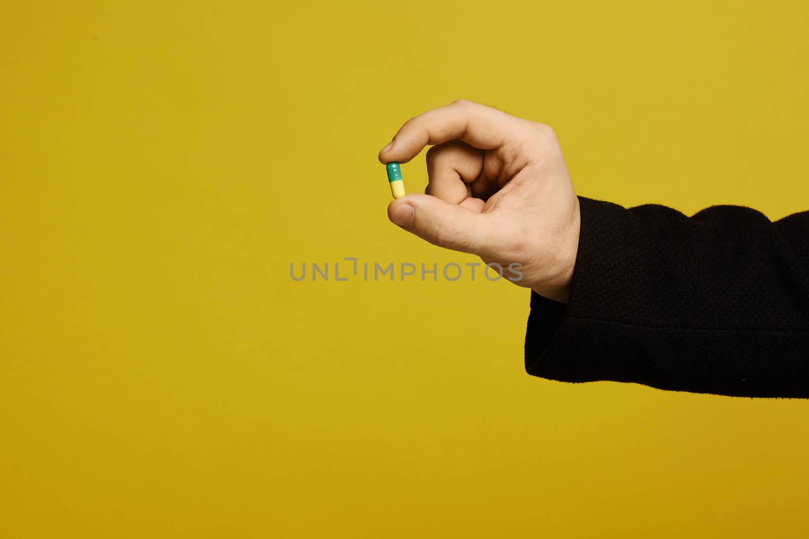 Yellow and green pill in the male hand on yellow background, isolated with copy space. Healthcare concept. Prevention infection, viruses and seasonal illness.